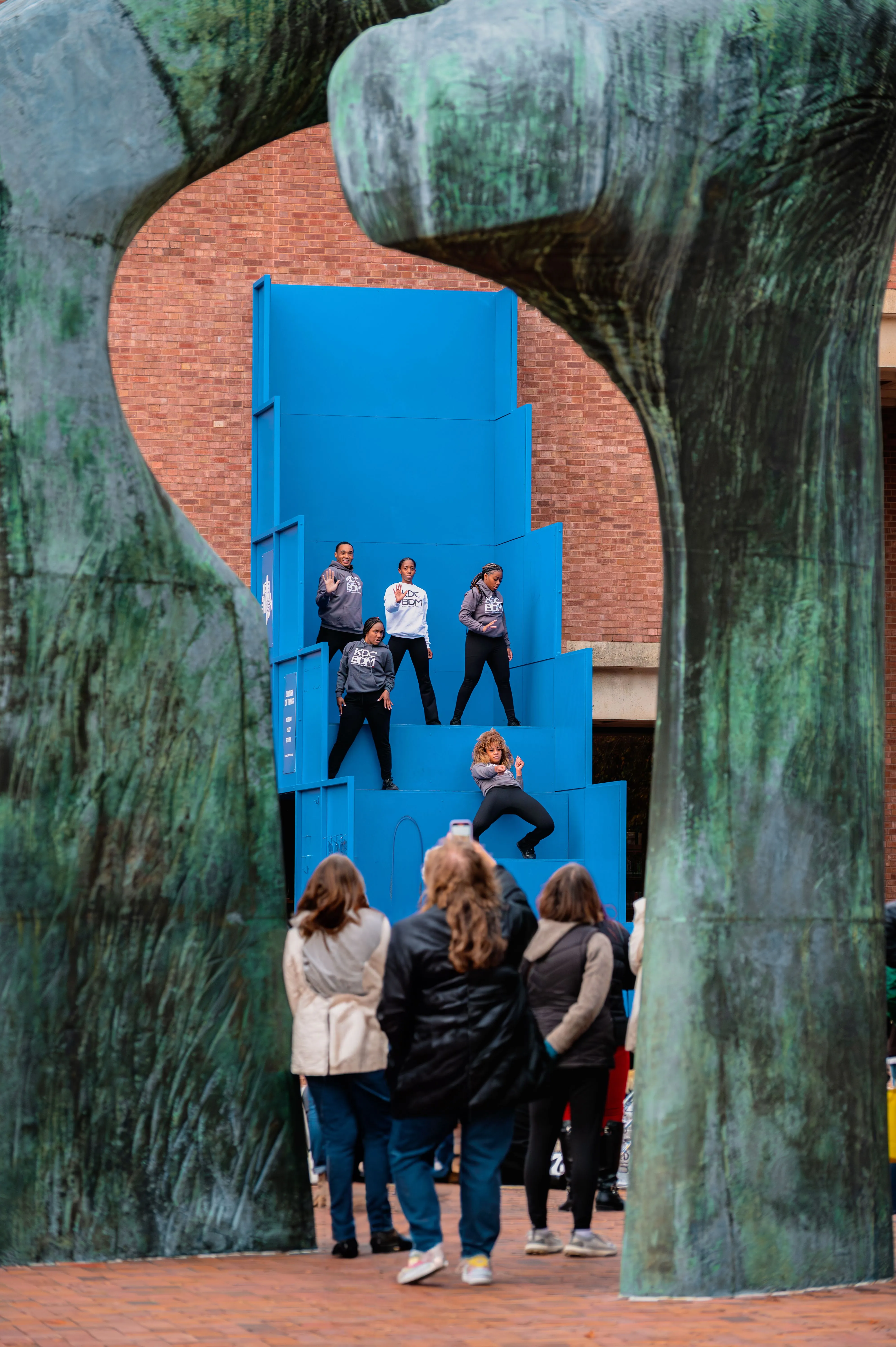 Group of people observing a blue art installation with a mirrored surface on an outdoor wall.