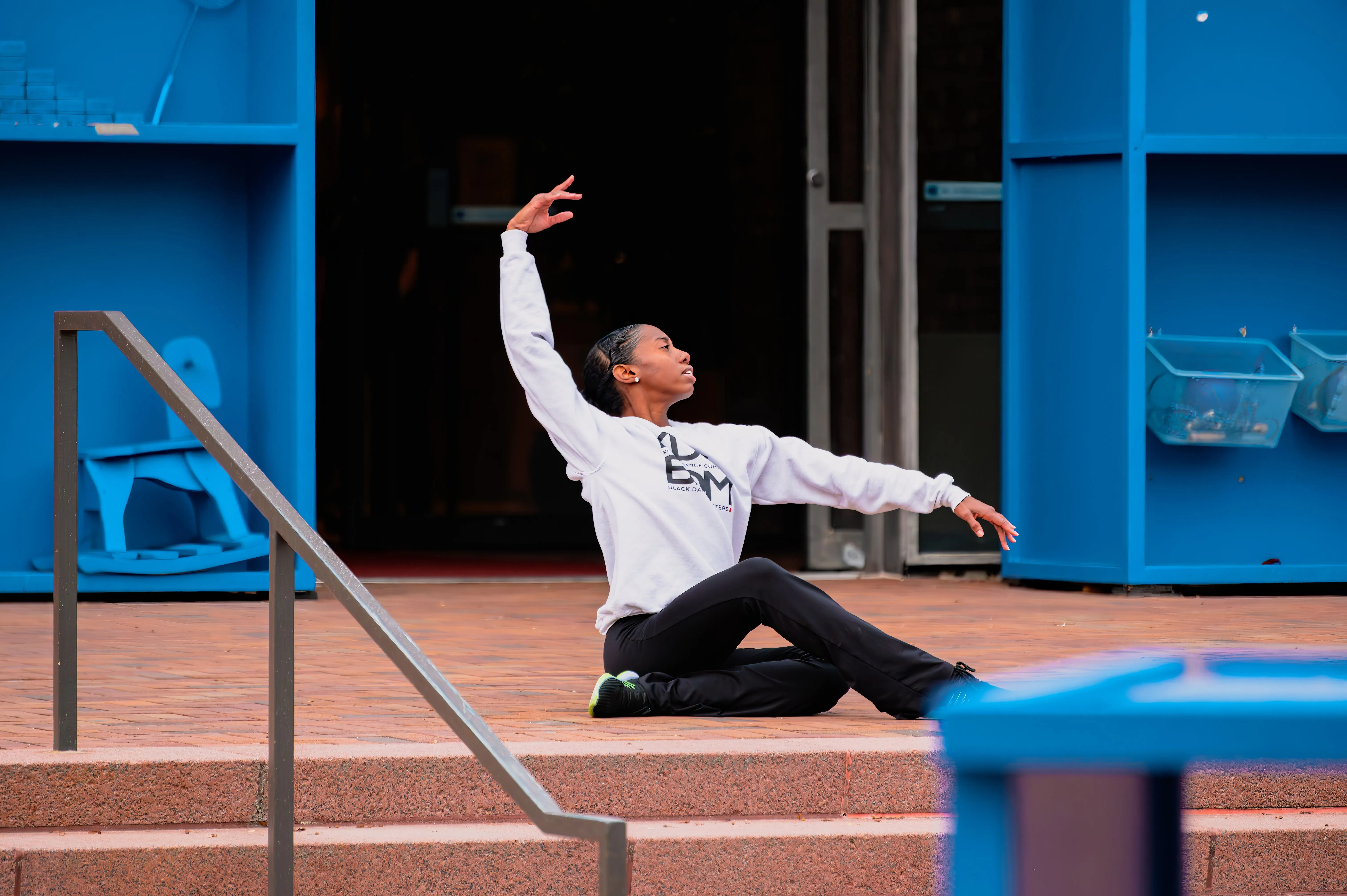 Person performing a dance move on outdoor stairs near a blue building.