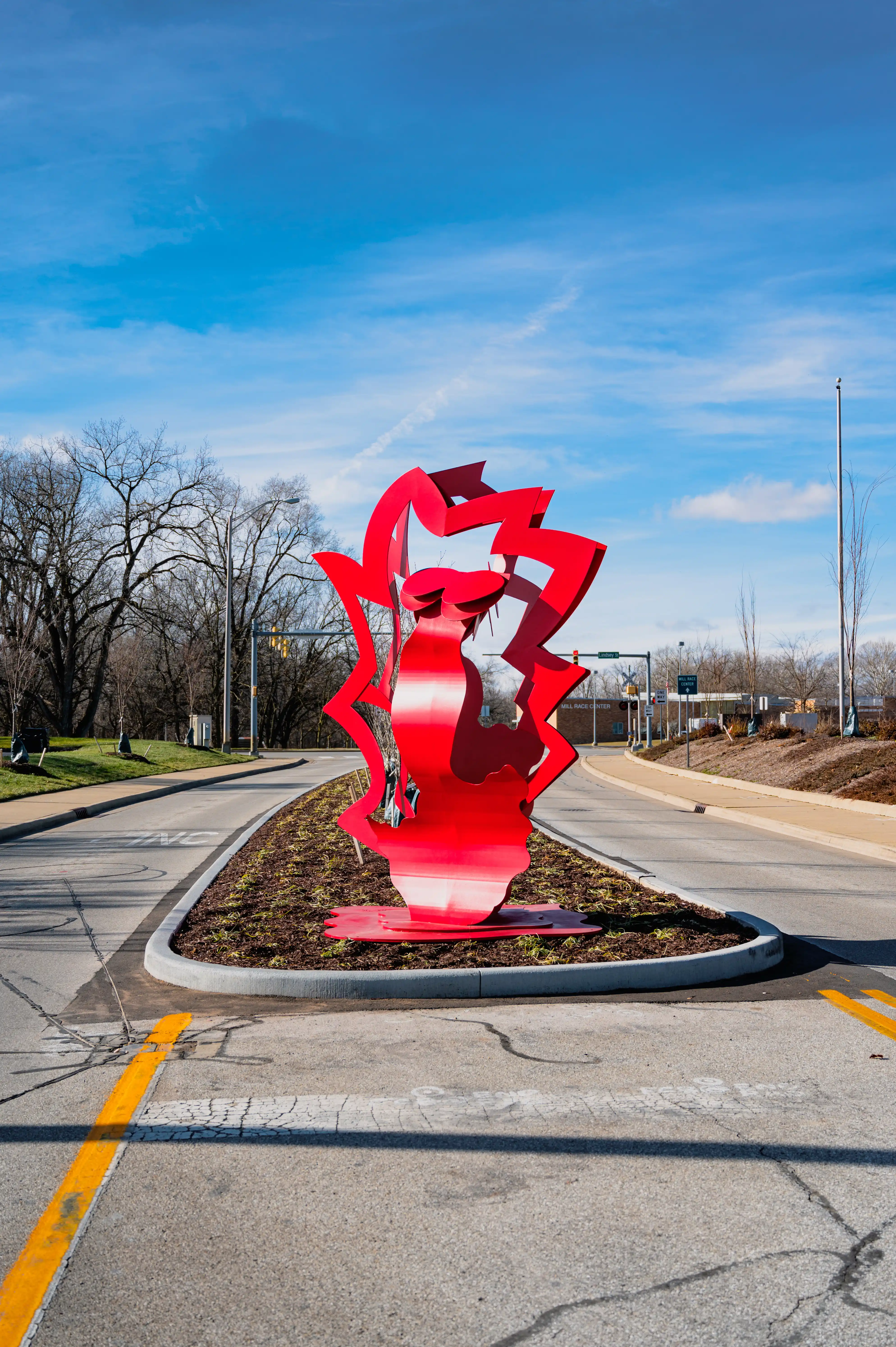 Red abstract sculpture at a road median under a clear blue sky.