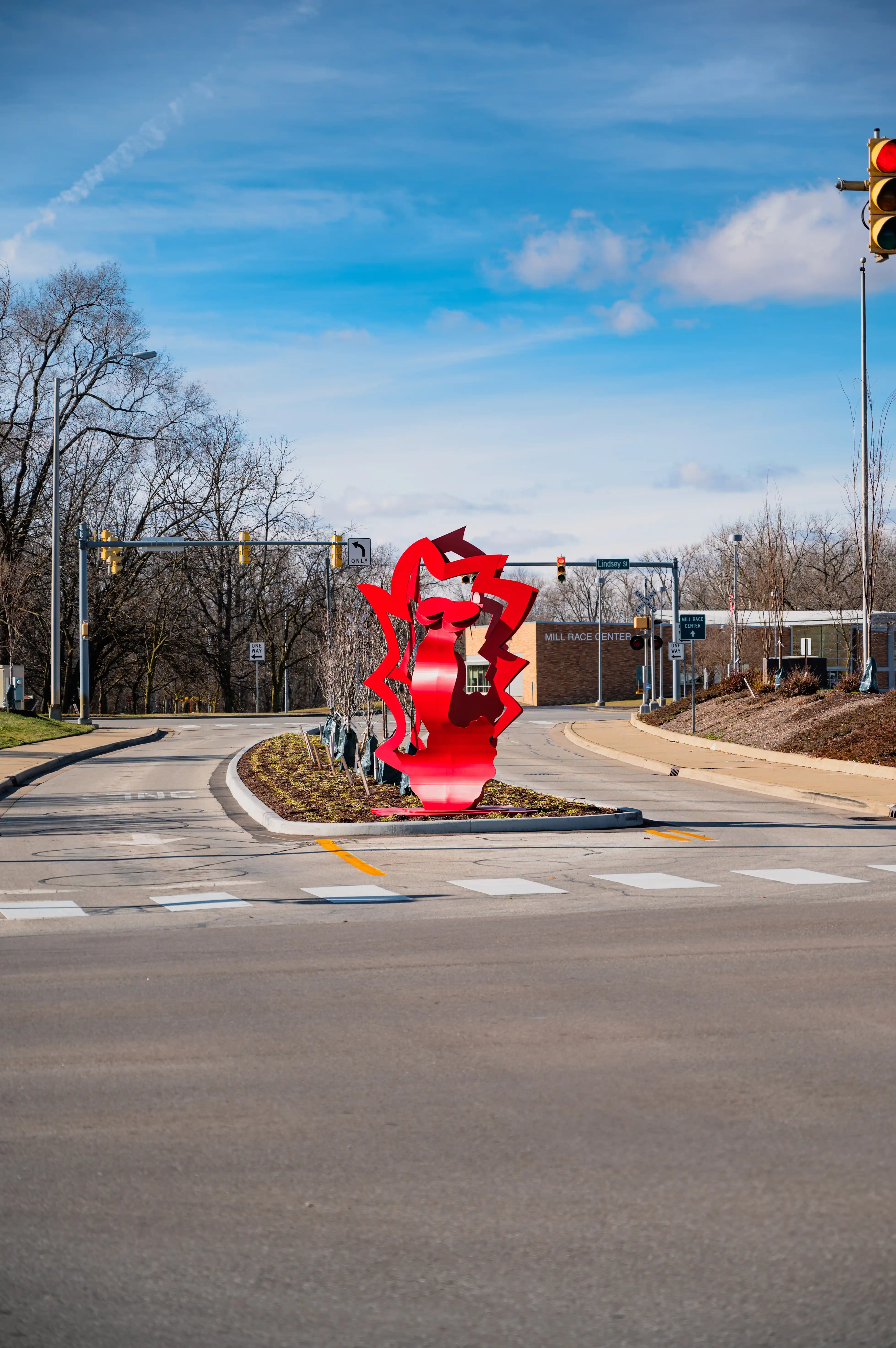 Red sculptural art piece in the shape of the number 8, located in the center of a traffic roundabout on a sunny day.