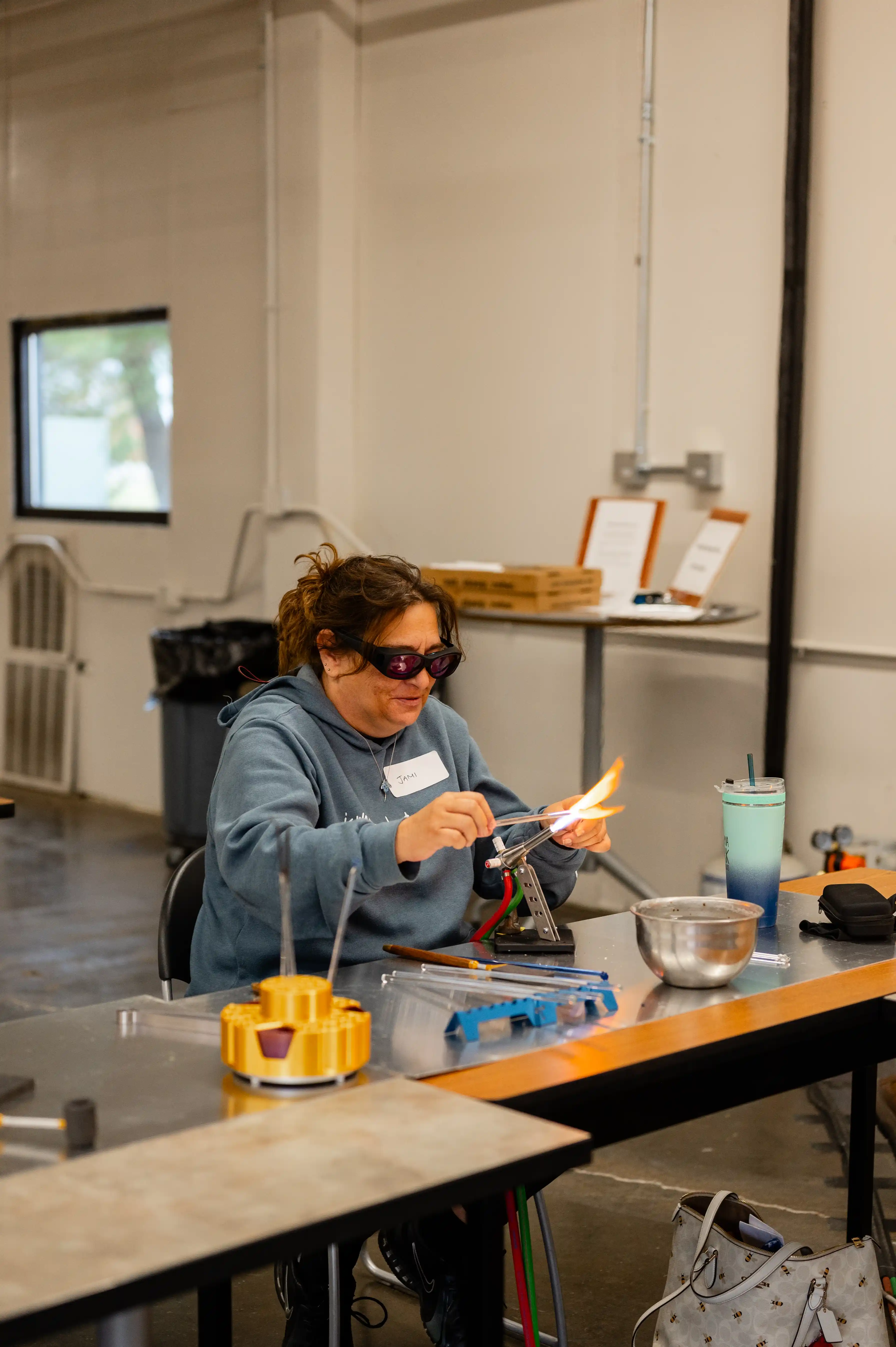 Person wearing safety goggles working with a glassblowing torch in a workshop setting.