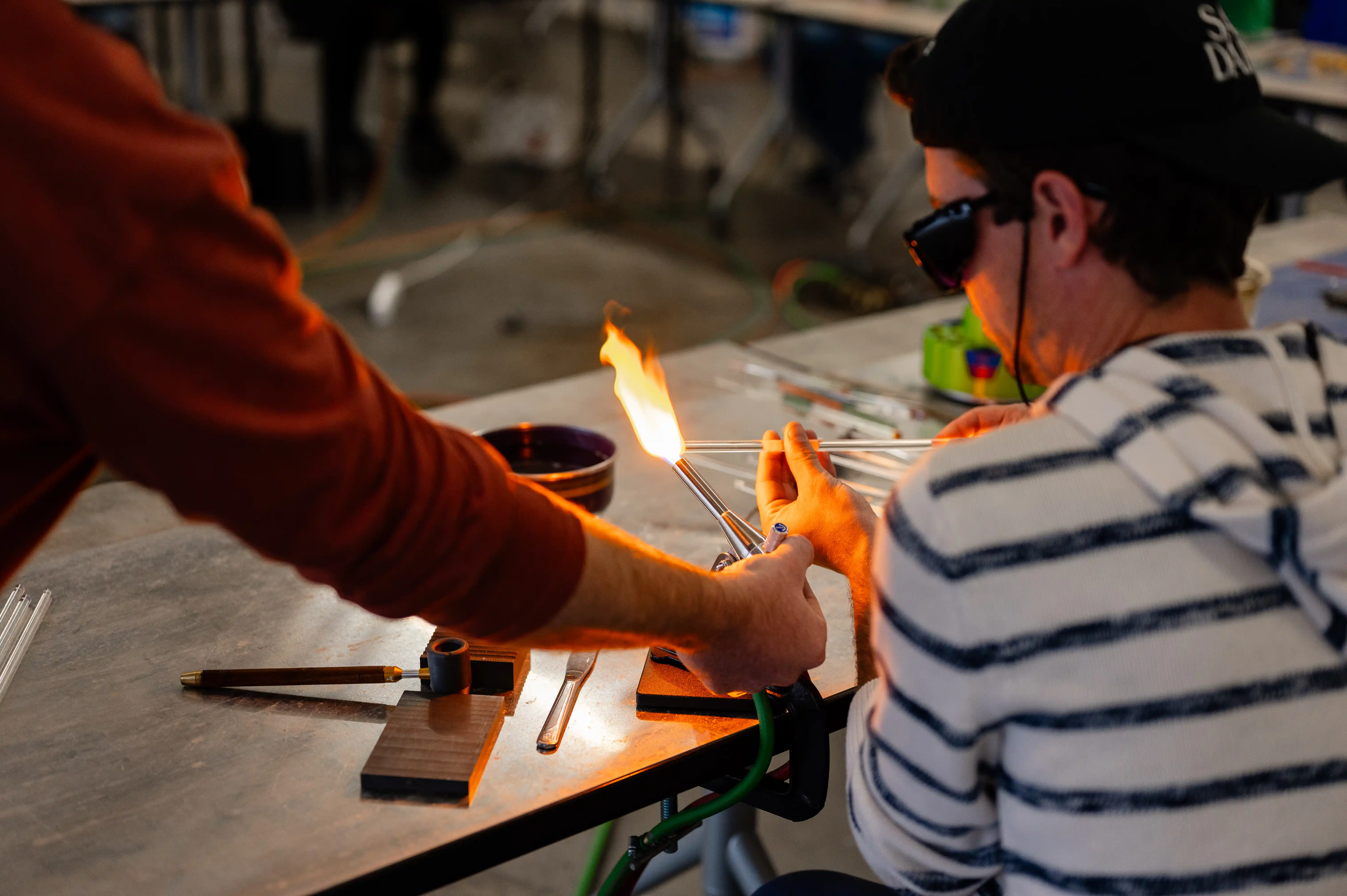 Two people shaping glass with a blowtorch in a workshop setting.