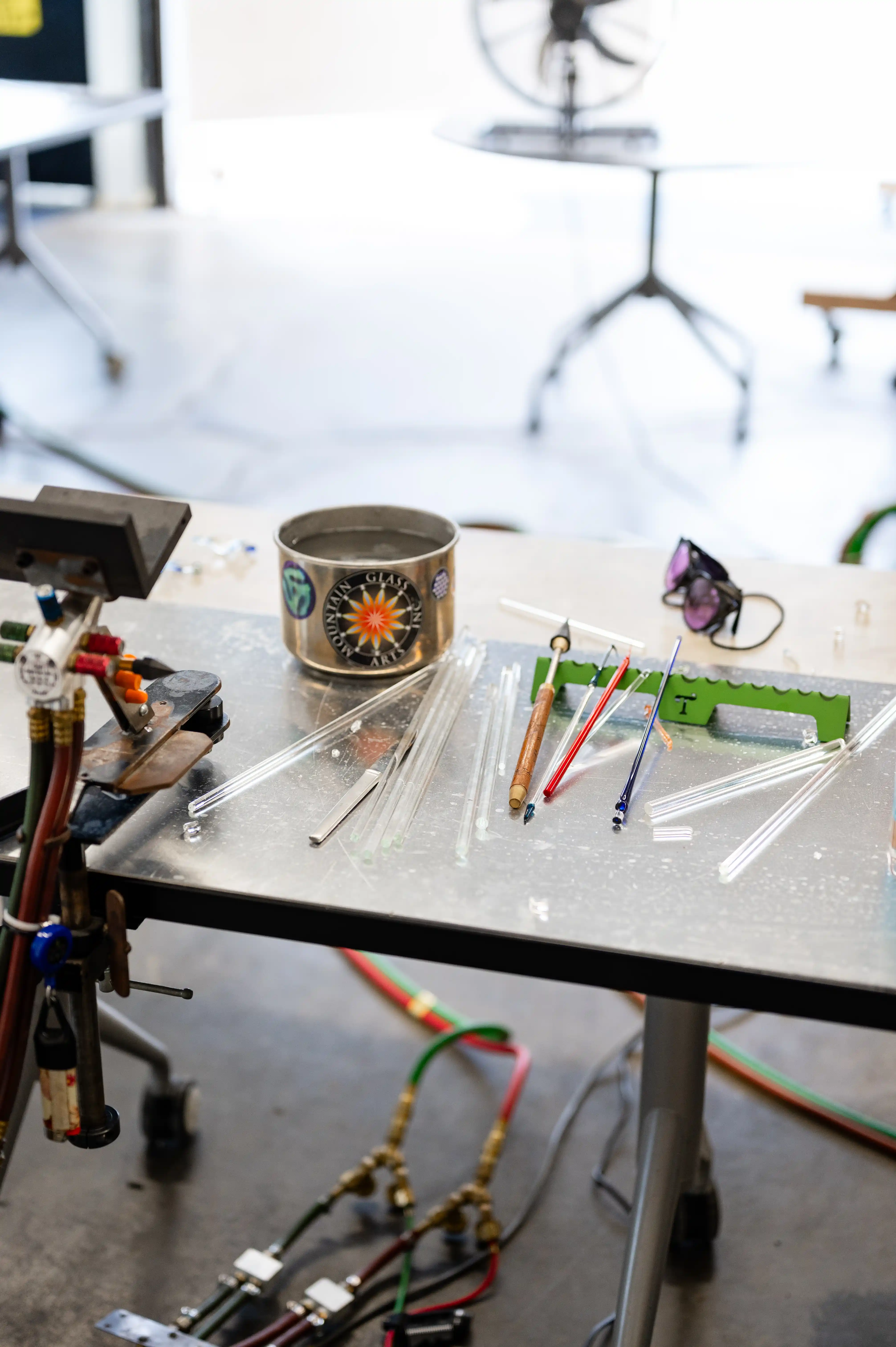 A glassblower's workbench with tools, glass rods, and a can with the studio's logo.