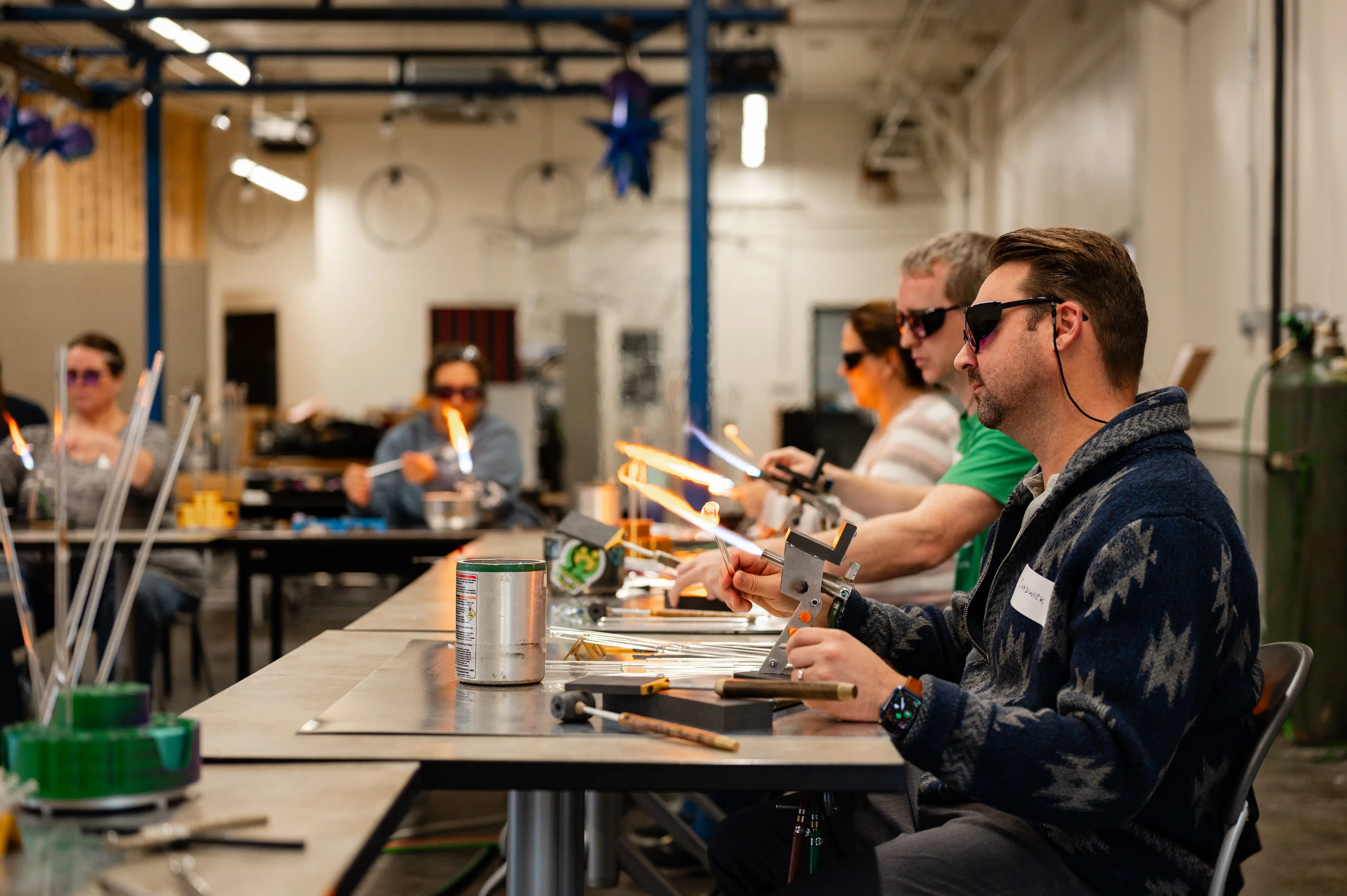People wearing safety glasses working with glass blowing torches at a glassblowing workshop.
