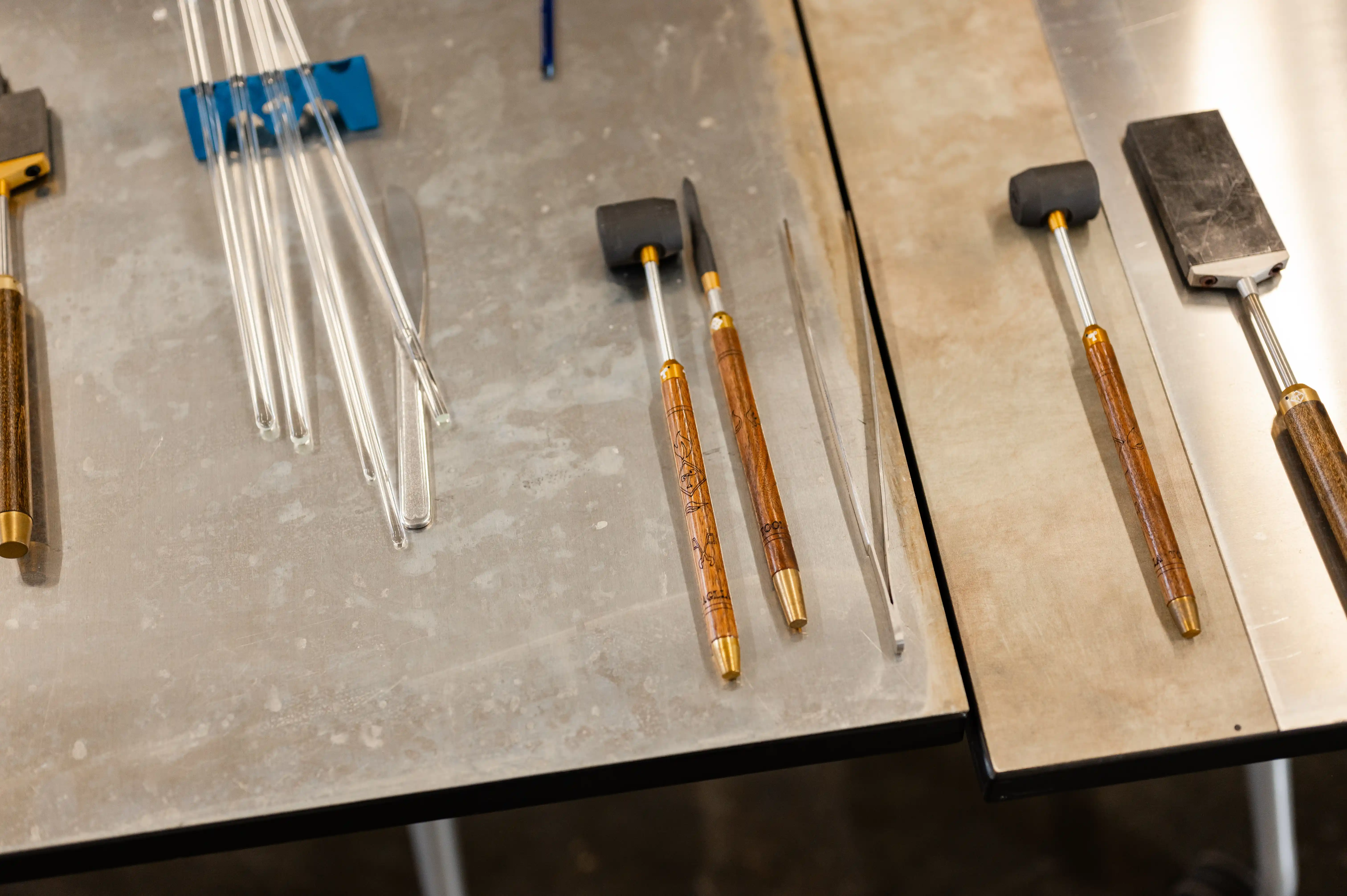 Glassblowing tools including tweezers, paddles, and jacks organized on a metal workbench.