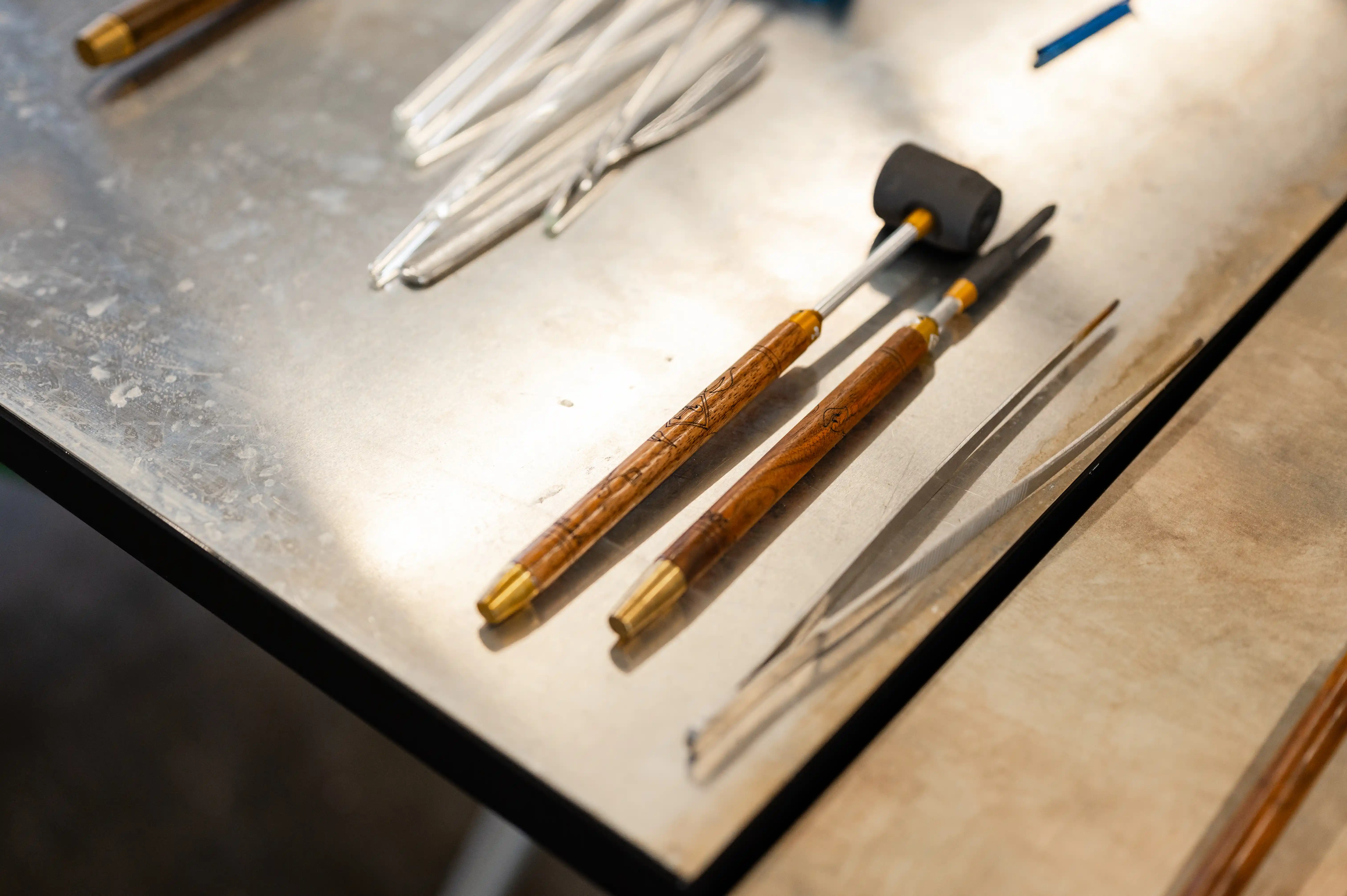 Assorted jewelry making tools including metal files and a hammer on a workbench.