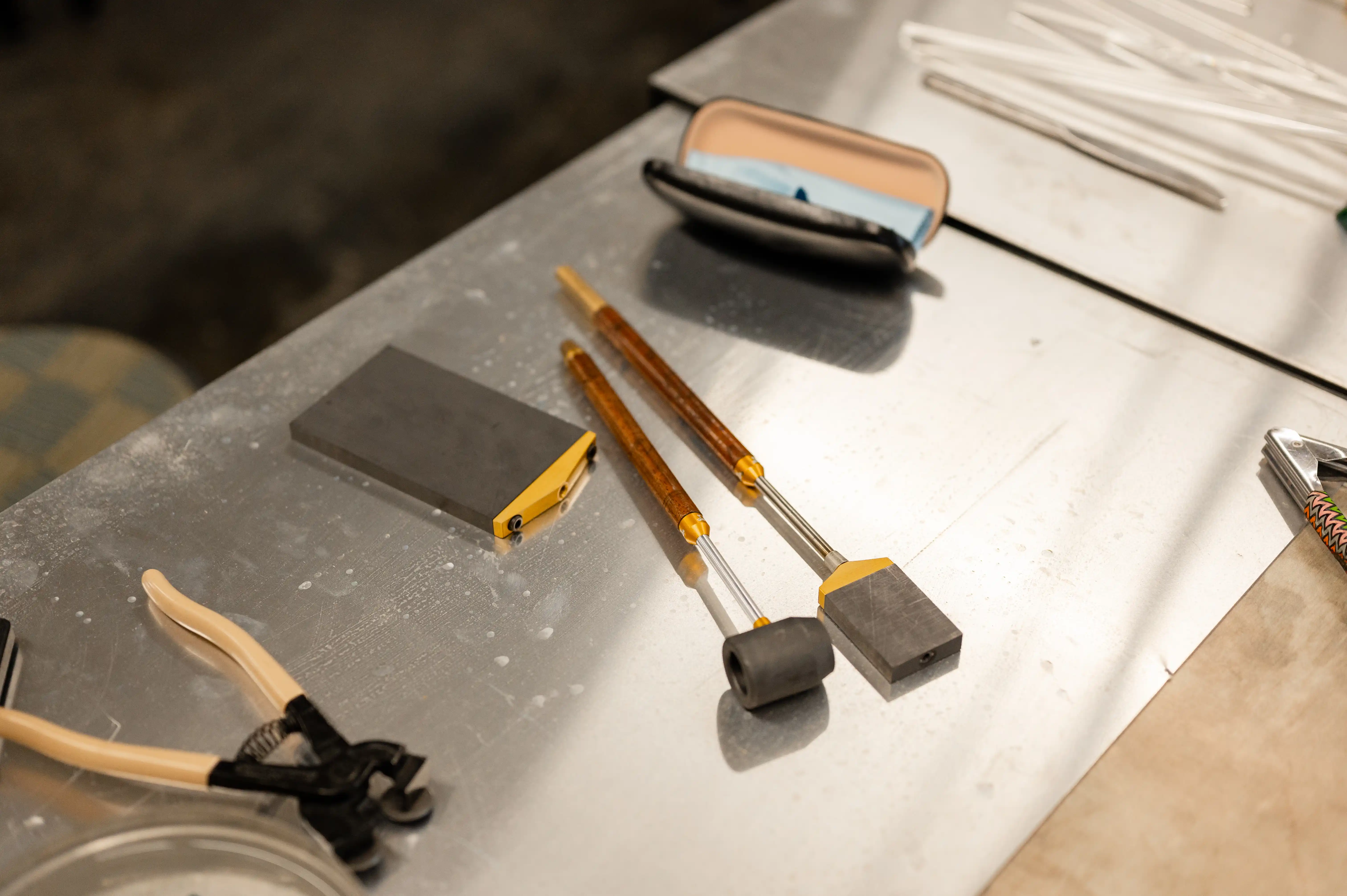 Various jewelry-making tools laid out on a workbench, including hammers, pliers, and a whetstone.