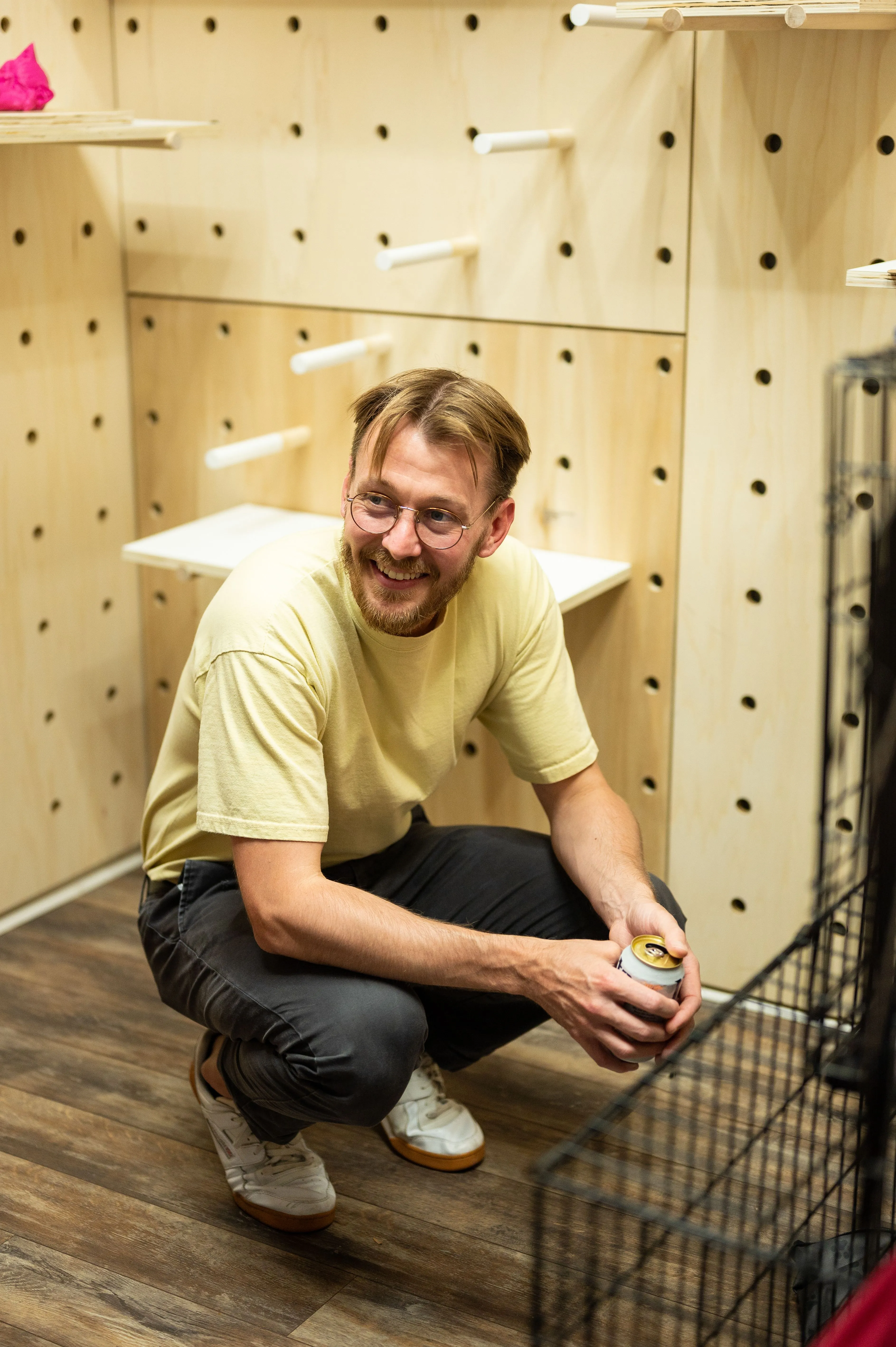 Man crouching and smiling inside a small wooden enclosure with pegboard walls.