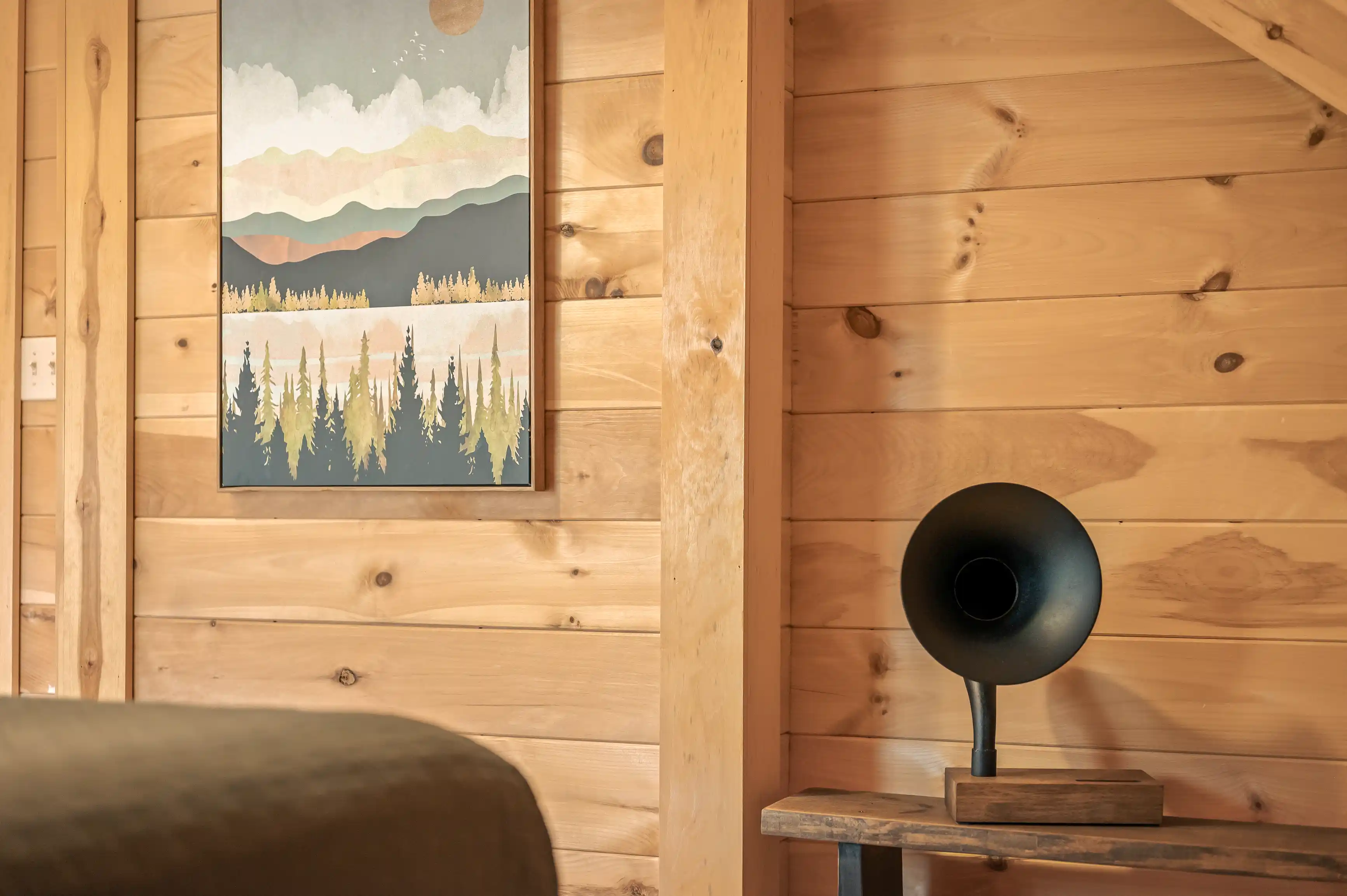 Cozy wooden cabin interior with a framed artistic nature landscape on the wall and a stylish black speaker on a wooden table.