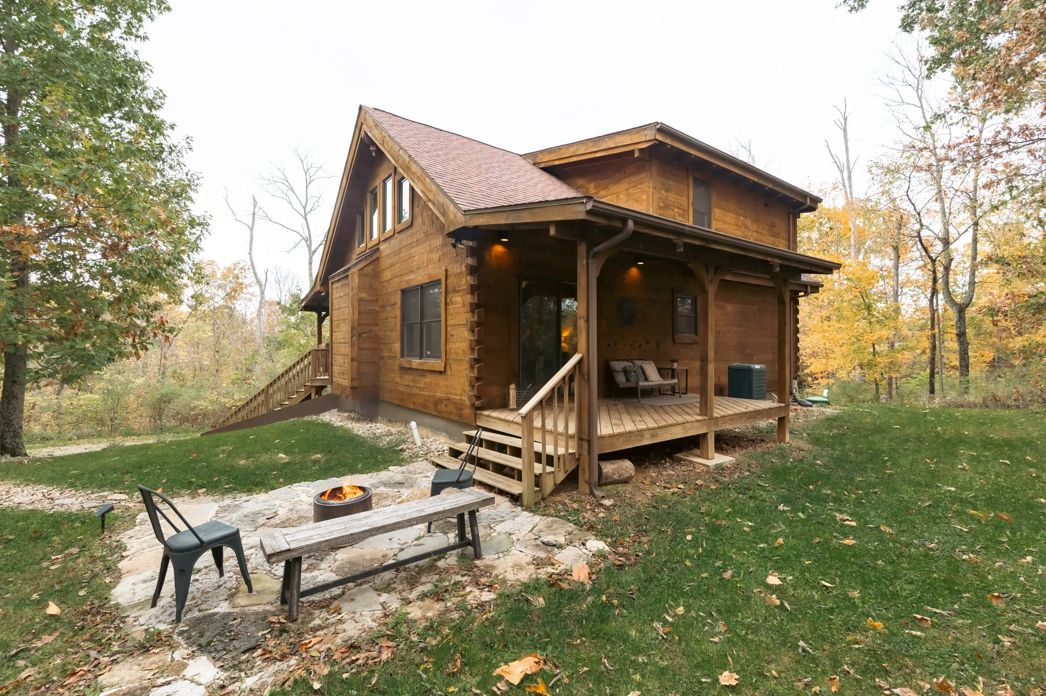 Rustic wooden cabin with a porch and outdoor fire pit surrounded by autumn foliage.