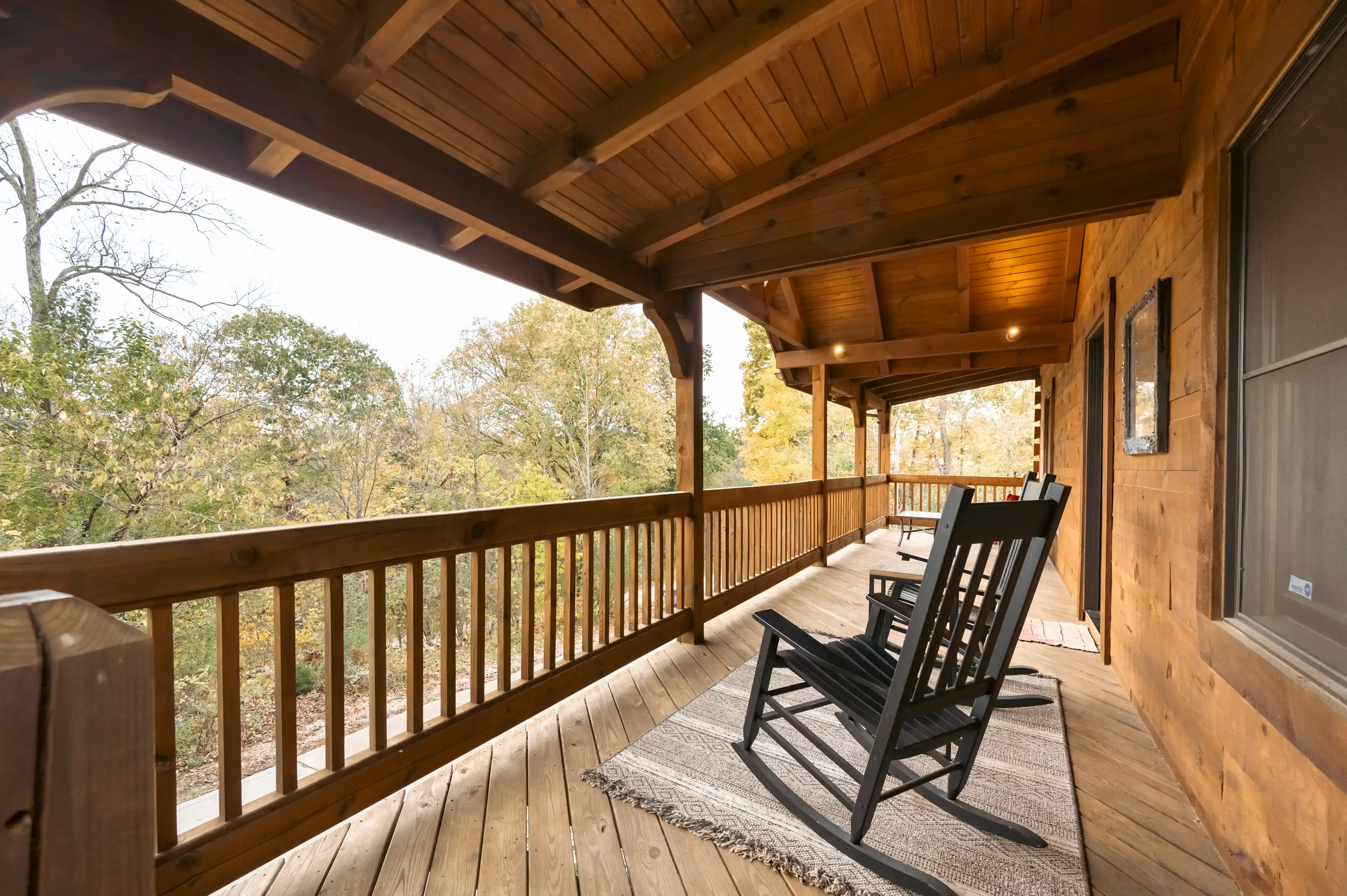 Spacious wooden deck of a rustic house with outdoor furniture and a view of autumn trees.