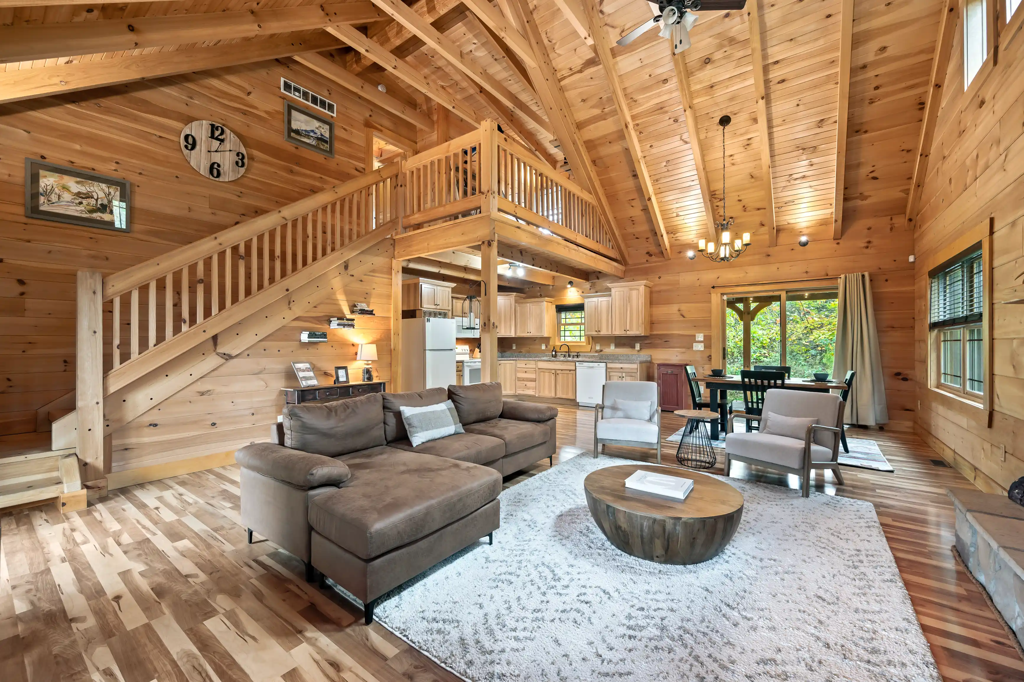 Spacious wooden cabin interior with high ceilings, loft area, open concept living room and kitchen, large sectional sofa, and rustic decor.