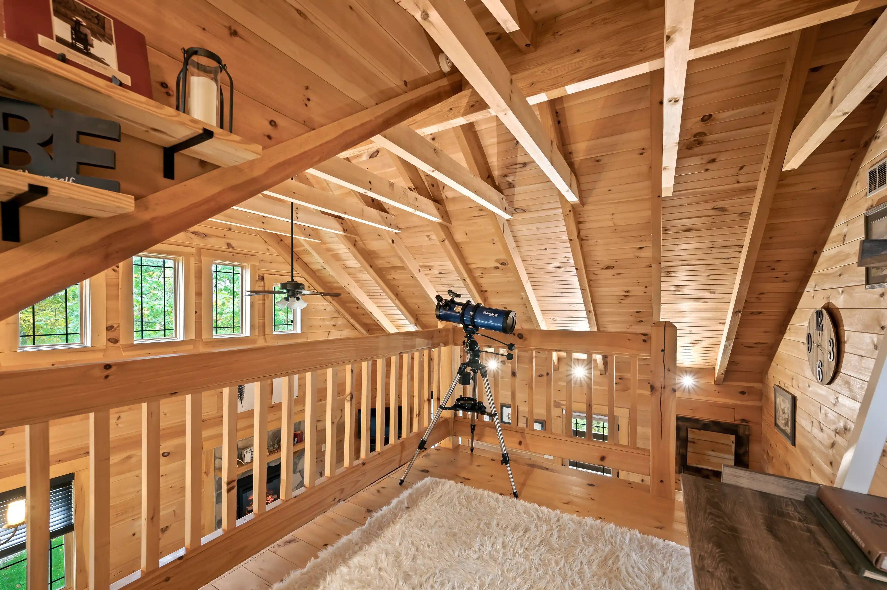 Cozy wooden attic space with exposed beams, telescope on a tripod, decorative lighting, and a glimpse of greenery through the windows.