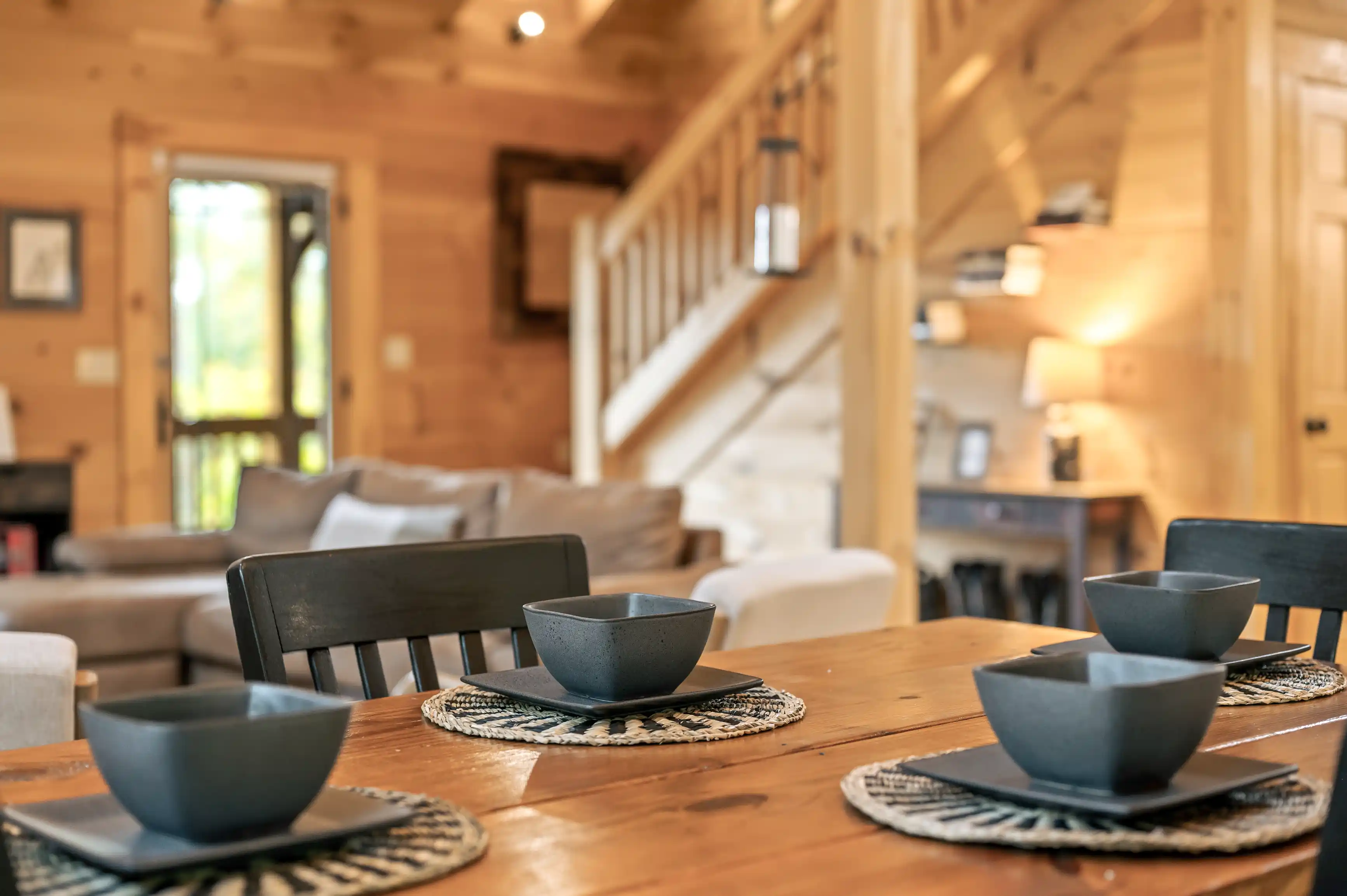 Cozy wooden cabin interior with focus on dining table set for two and blurred background featuring living area and stairs.