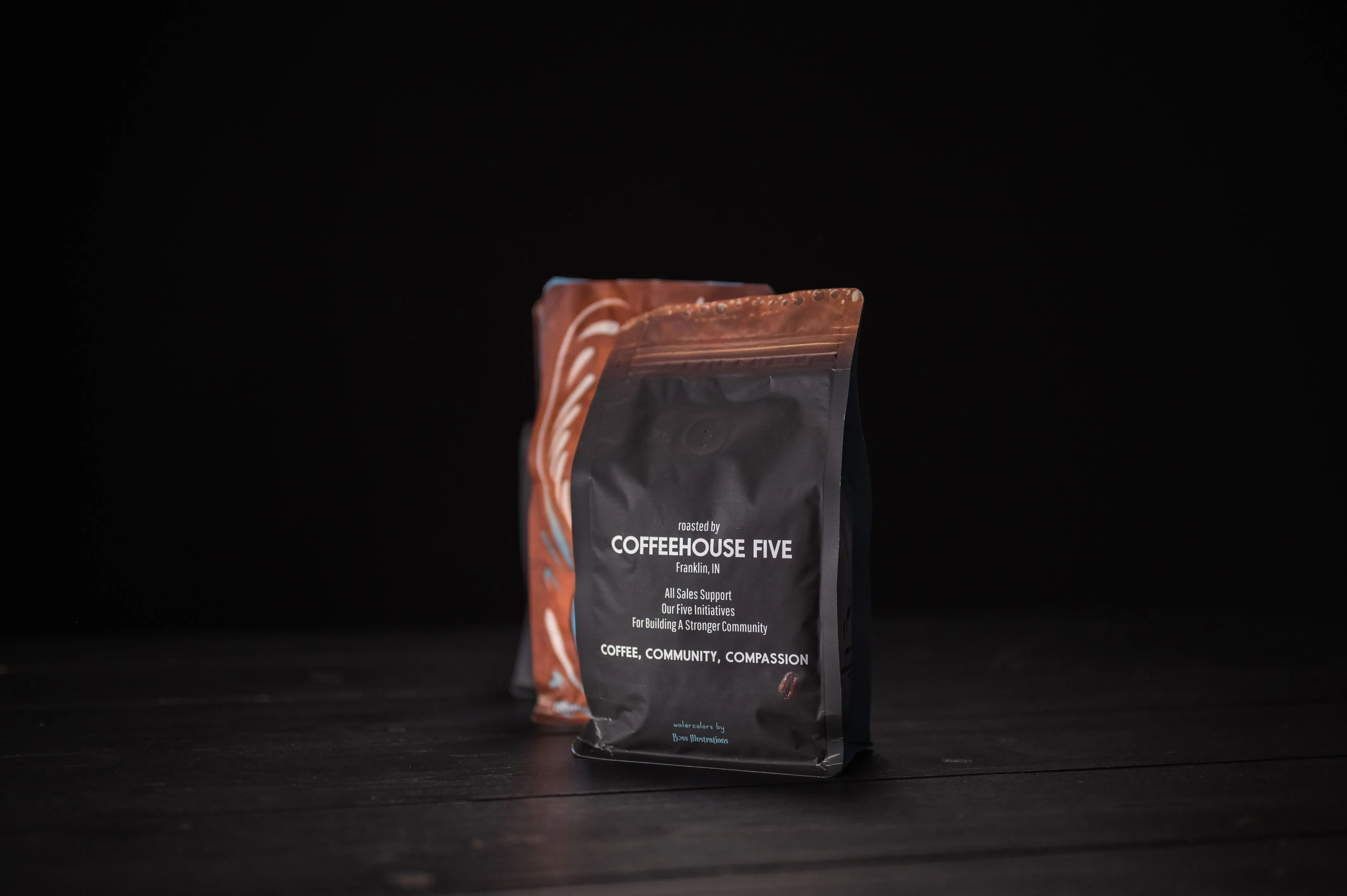 Sealed bag of Coffeehouse Five coffee on a dark wooden surface against a black background.