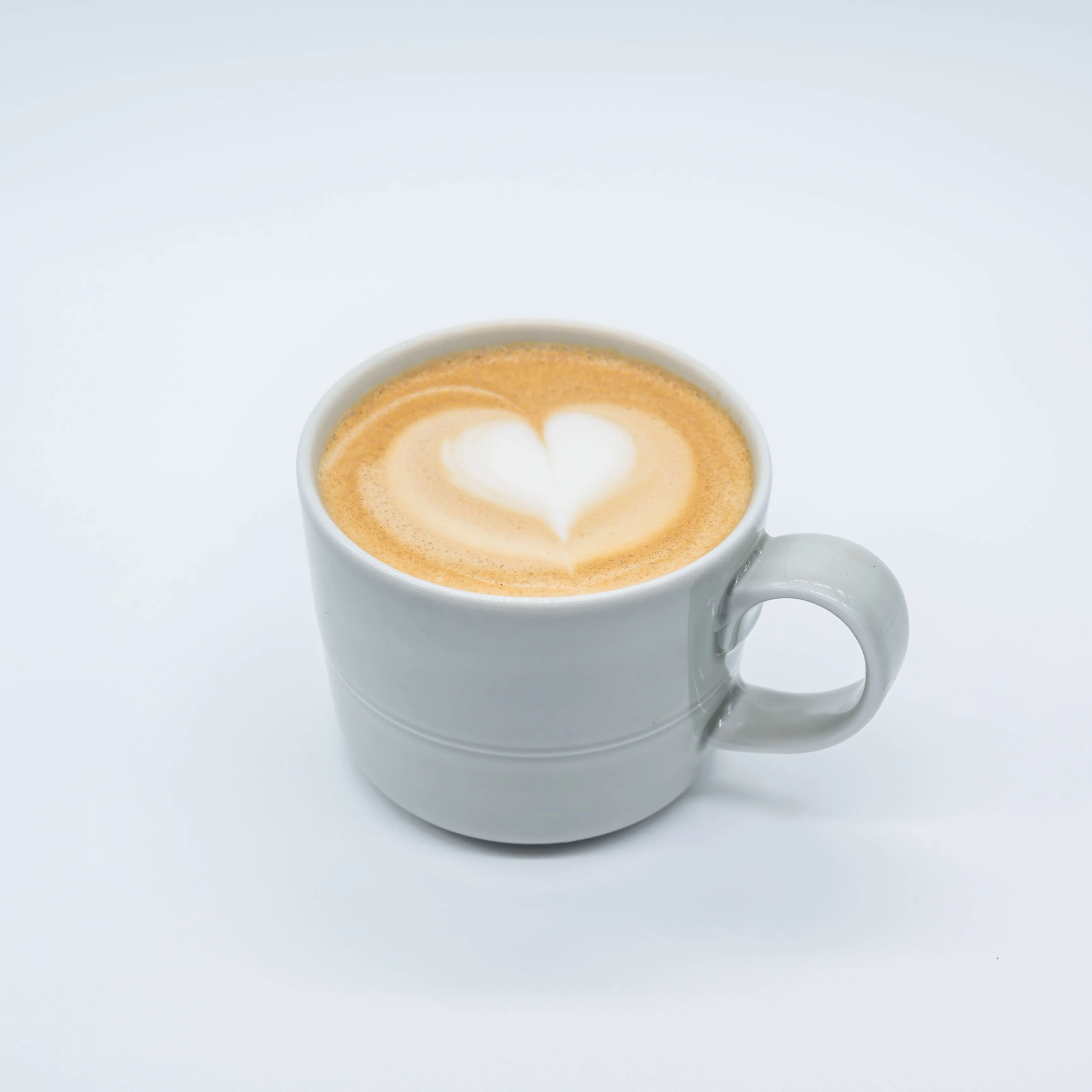 A cup of cappuccino with heart-shaped latte art on a white background.