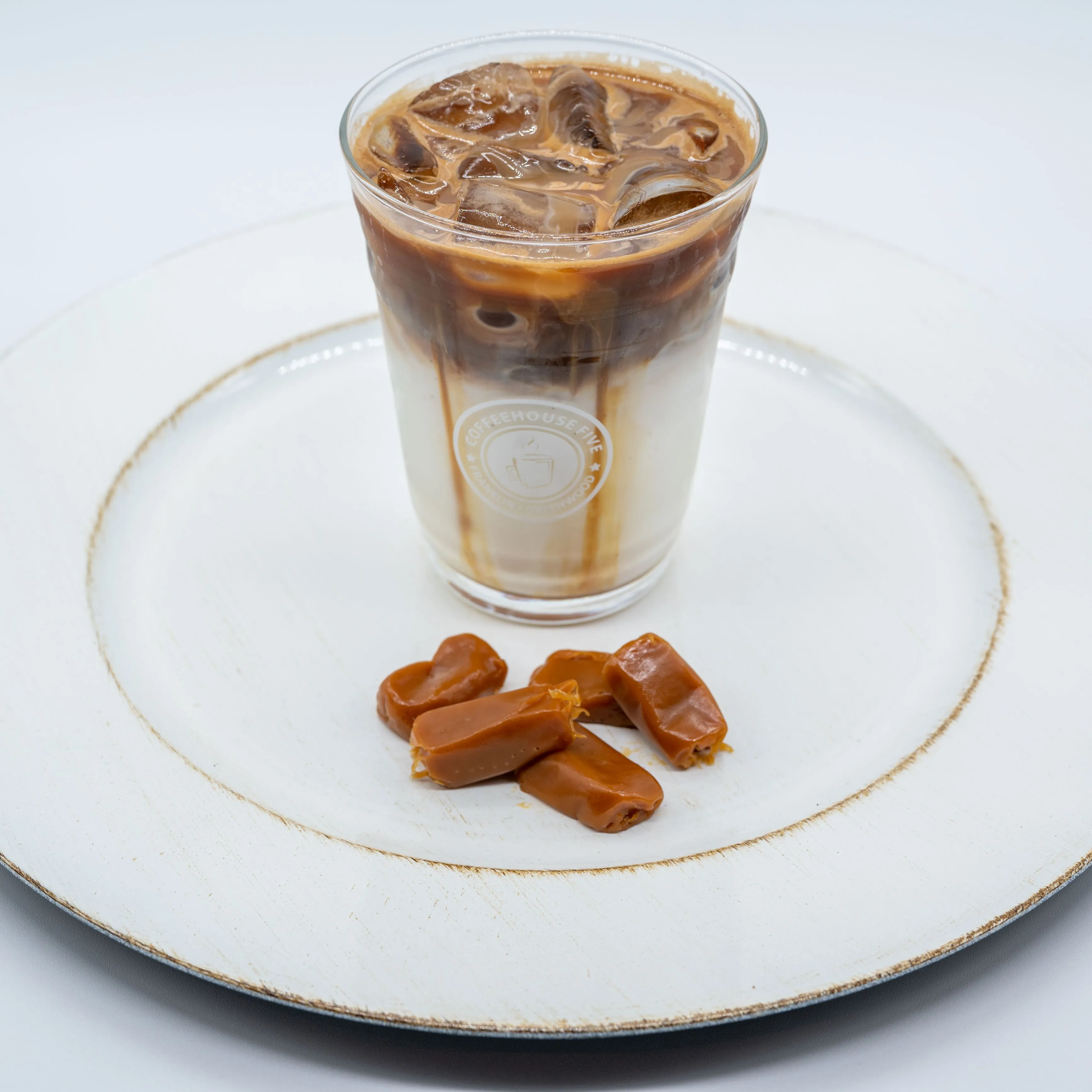 Iced caramel macchiato in a clear glass on a ceramic plate with caramel candies.