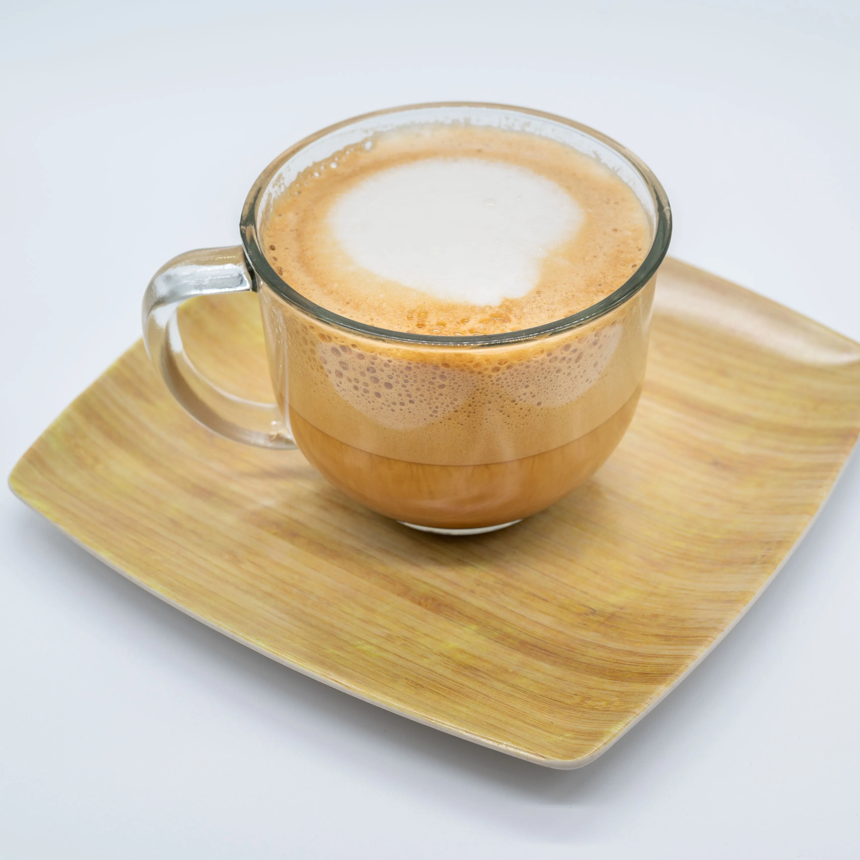 A cup of cappuccino with frothy milk on top, on a bamboo plate against a white background.