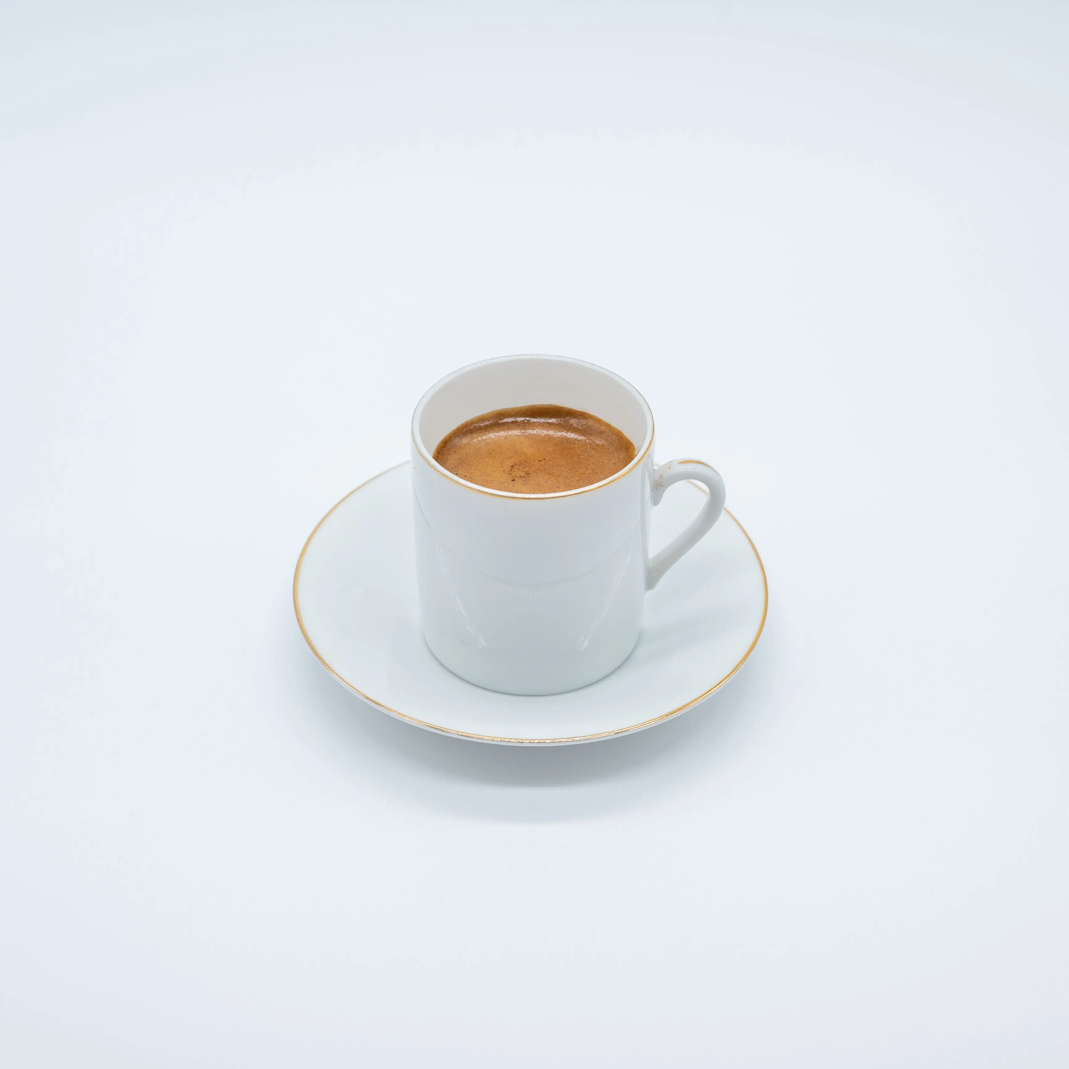 A white cup filled with espresso on a saucer, set against a white background.
