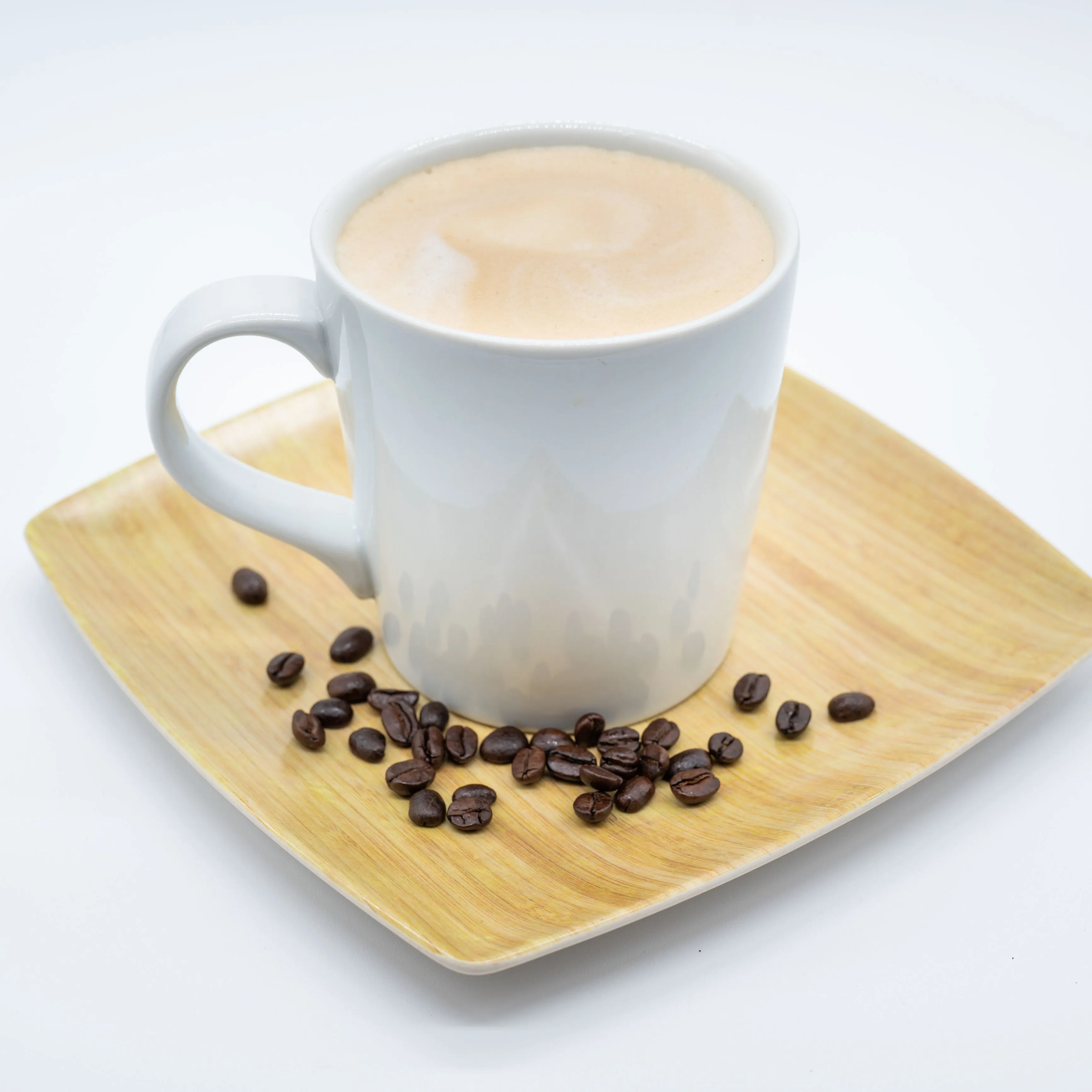 A cup of cappuccino on a wooden plate with scattered coffee beans beside it on a white background.
