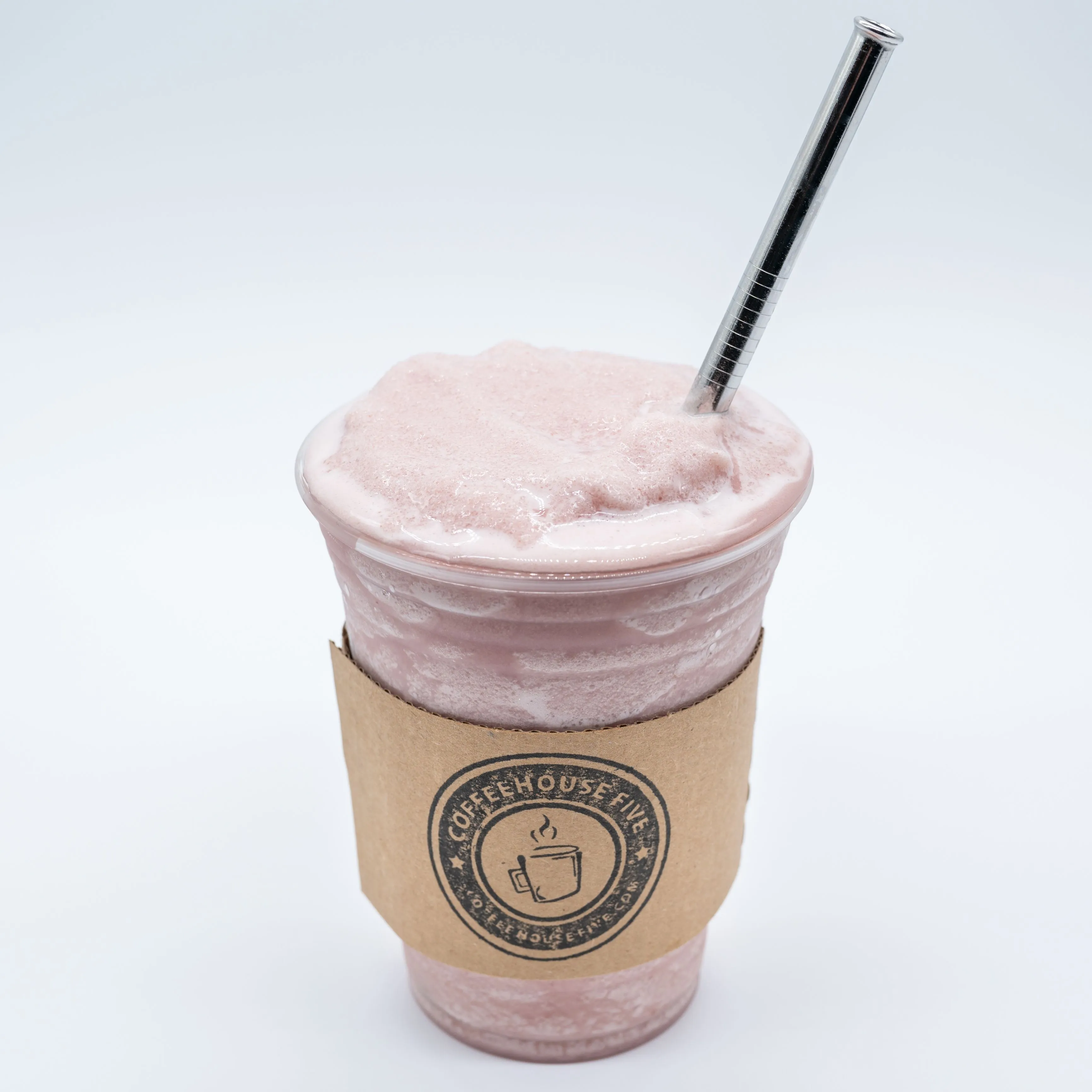 A frothy pink smoothie in a clear plastic cup with a cardboard sleeve and a metal straw, set against a white background.