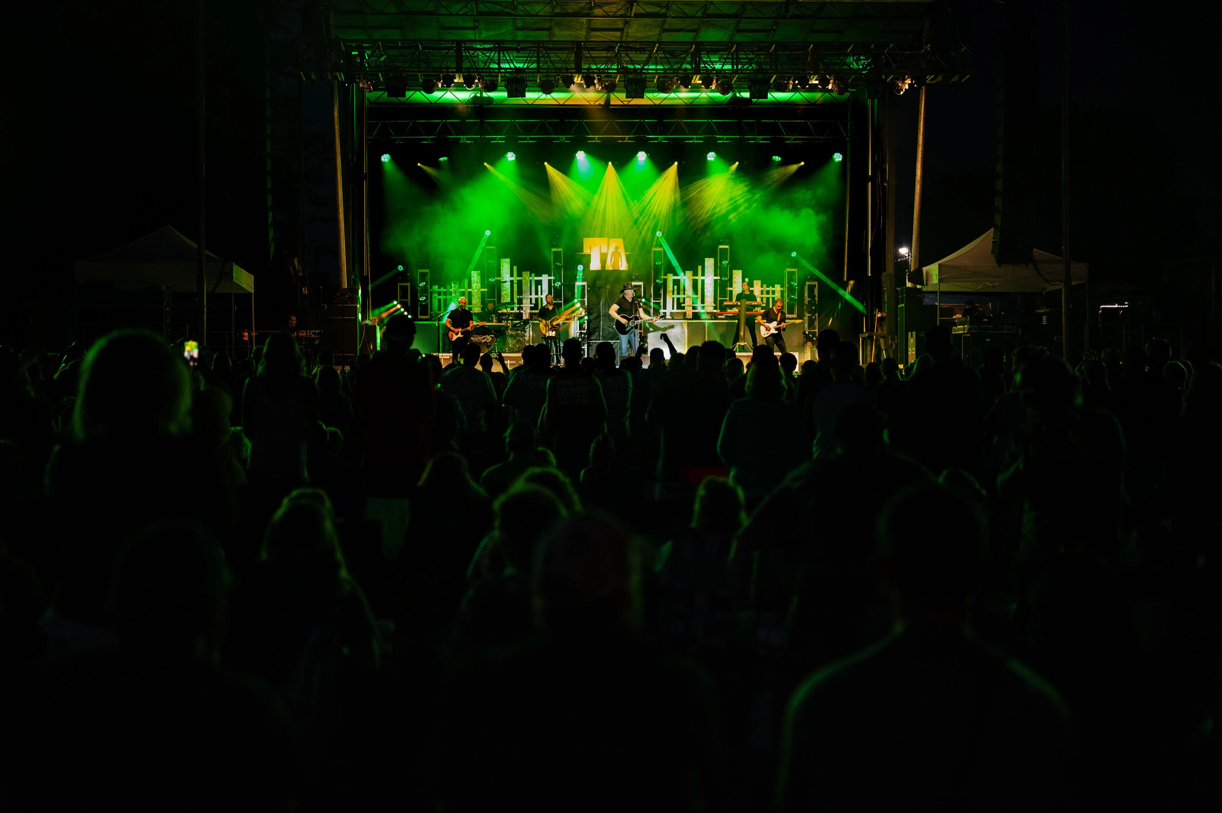 Crowd watching a live concert with a brightly lit stage under green lights.