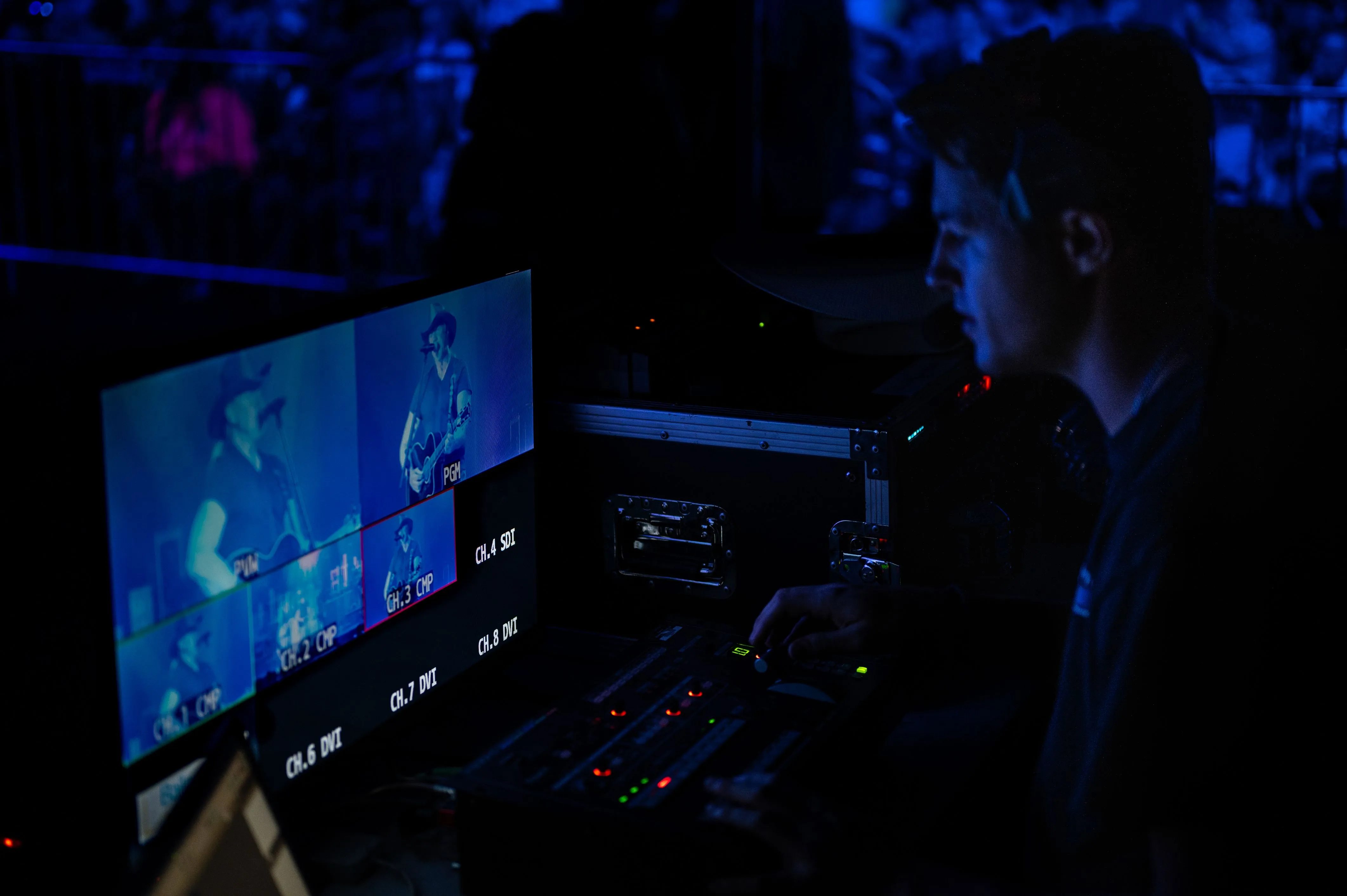 Person working with video equipment in a dark control room with multiple screens displaying images.