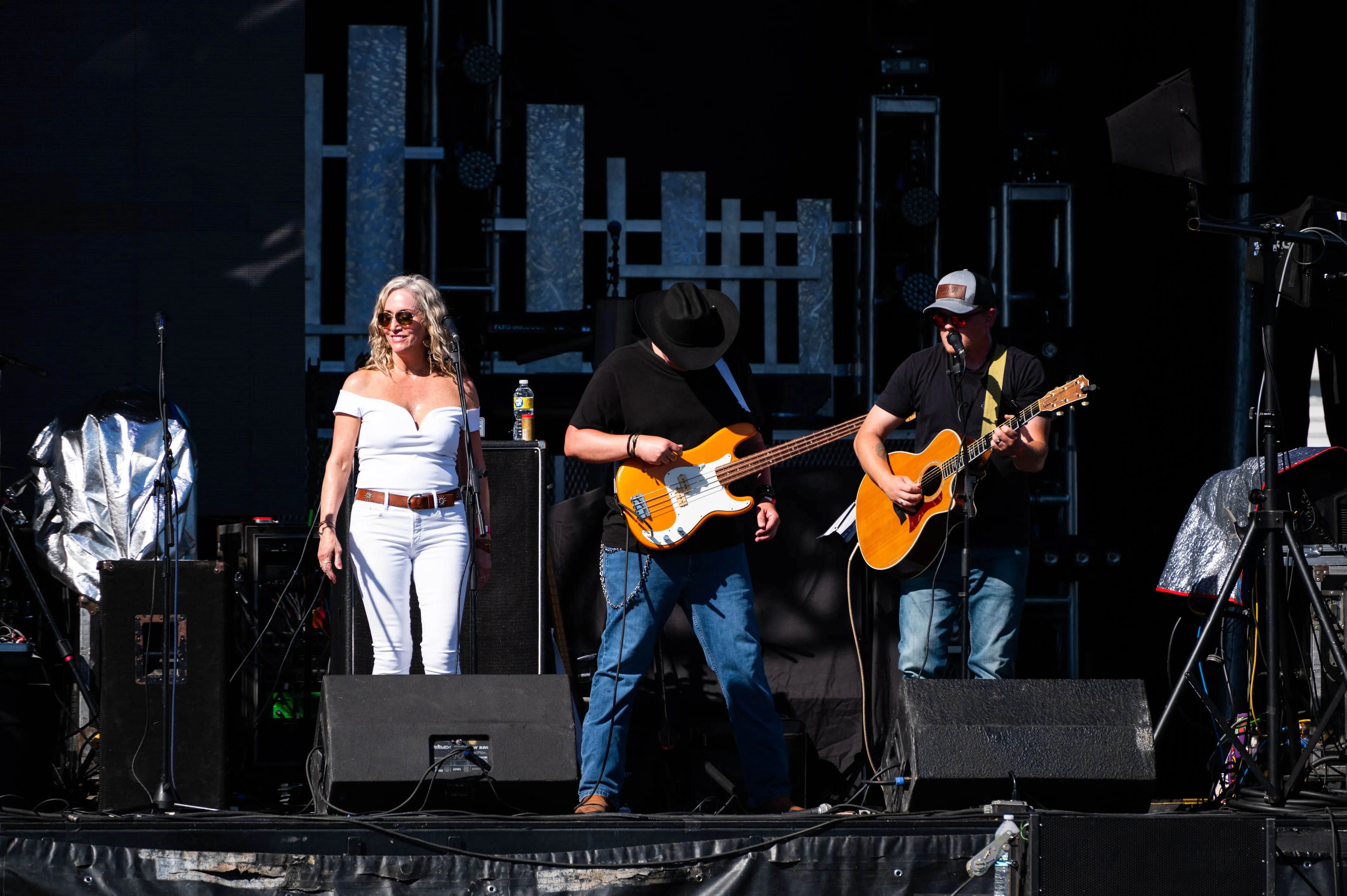 Three musicians performing on stage, with a female singer in the center and two guitarists on either side.