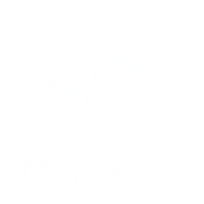 Logo of Cozy Cabins featuring an illustration of a cabin among pine trees with a crescent moon and stars overhead, with the text "Cozy Cabins Brown County Indiana" below.