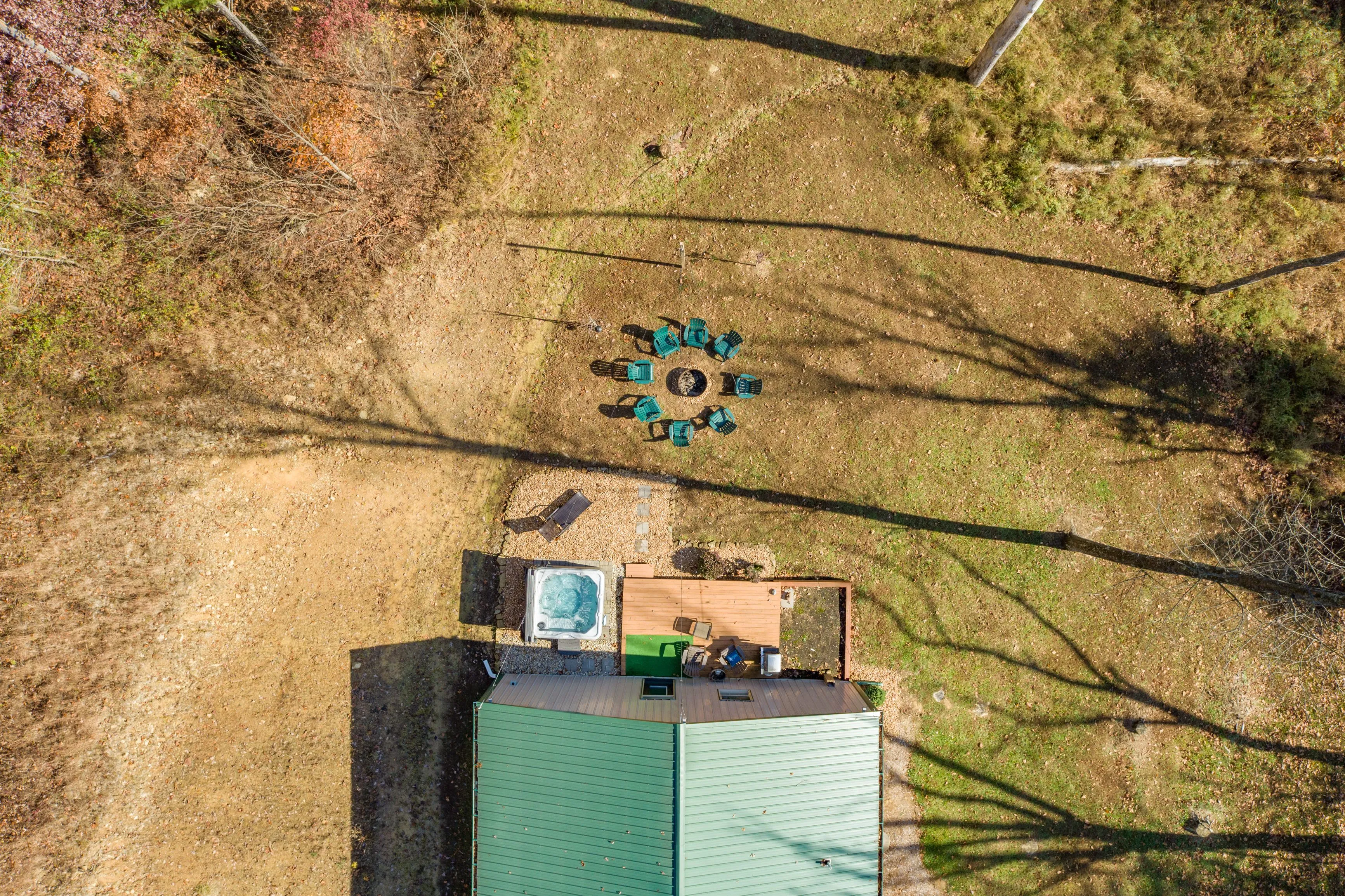 Aerial view of a backyard with a hot tub and a circular arrangement of chairs around a fire pit, casting long shadows.