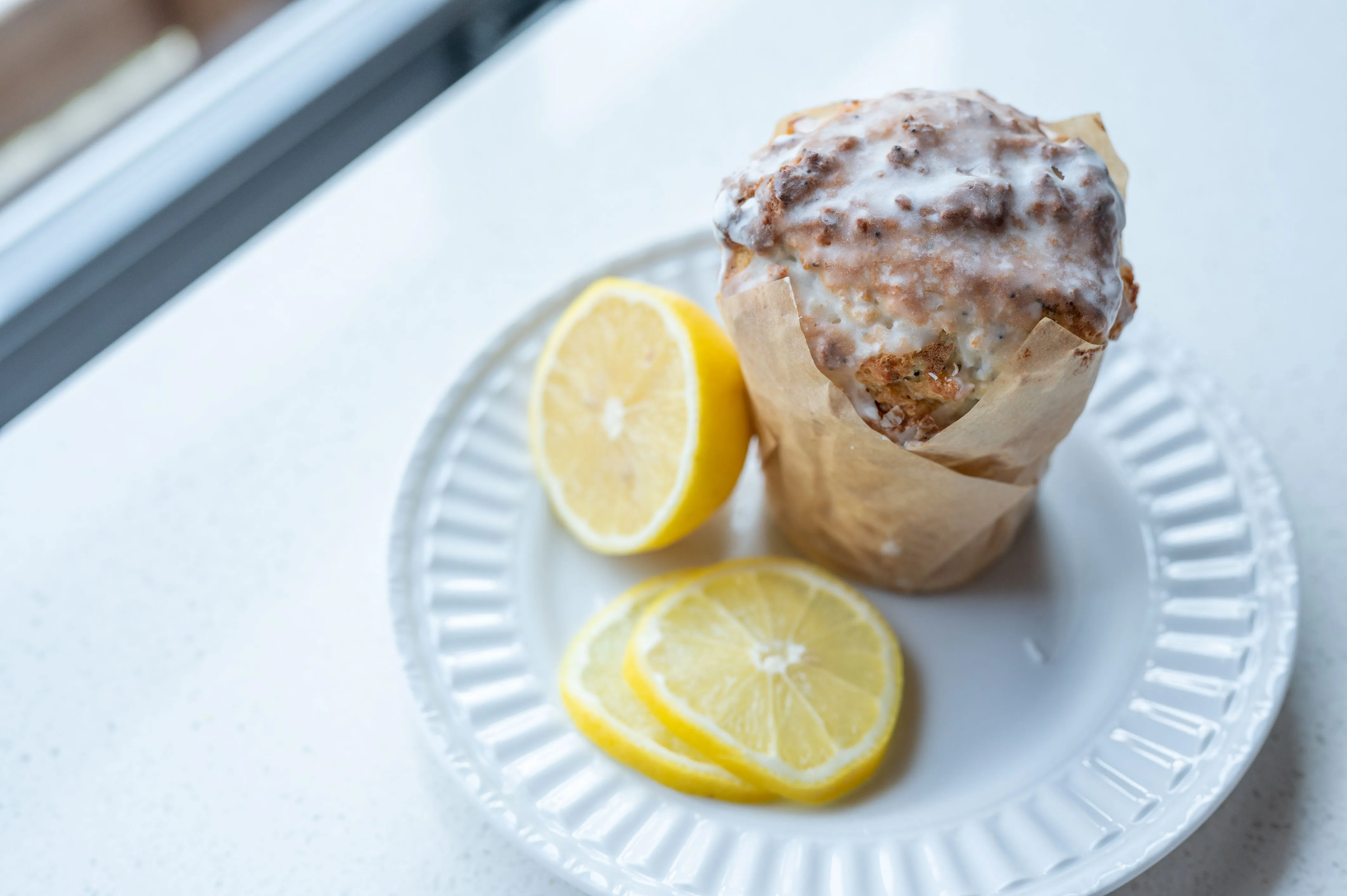 Lemon poppy seed muffin with icing on a white plate accompanied by sliced lemons.