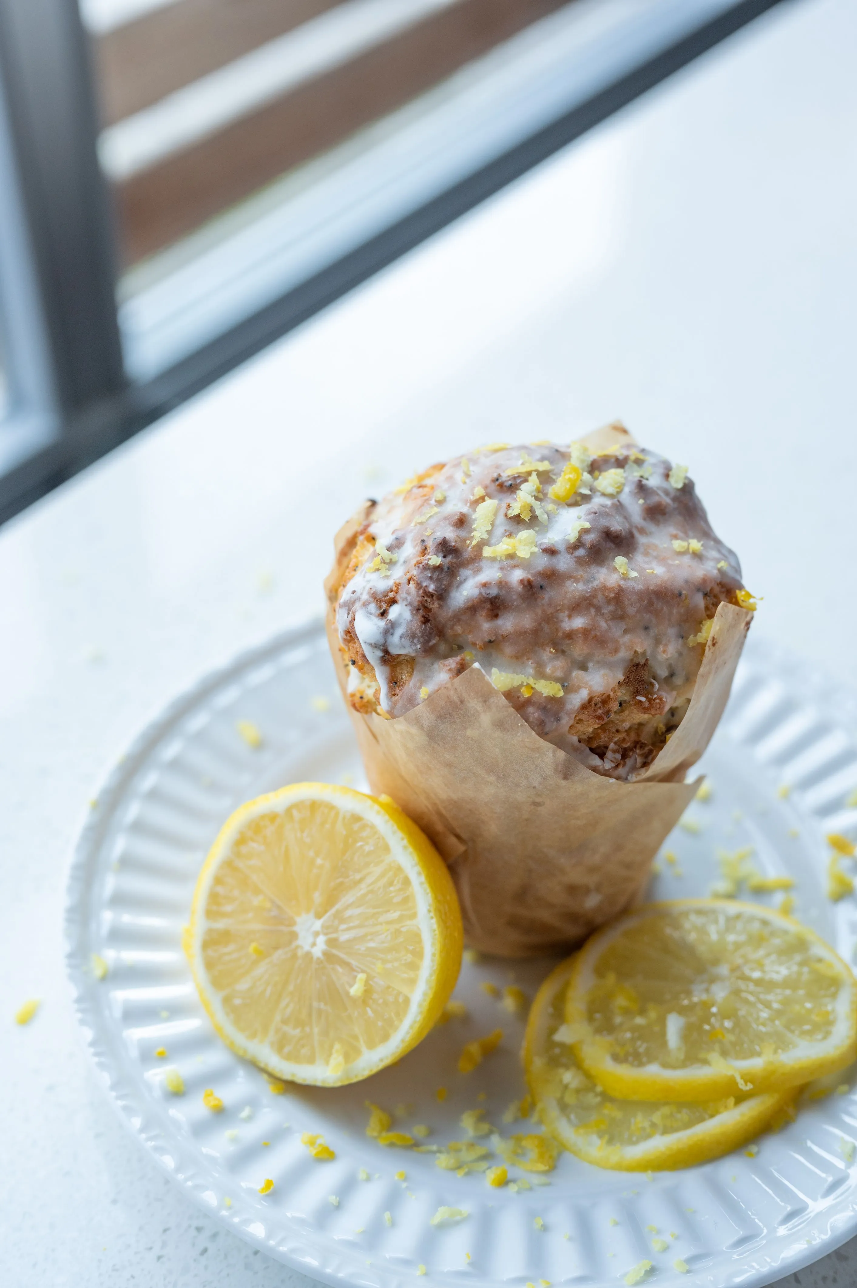 Lemon poppy seed muffin with glaze and lemon zest on a white plate with sliced lemons.