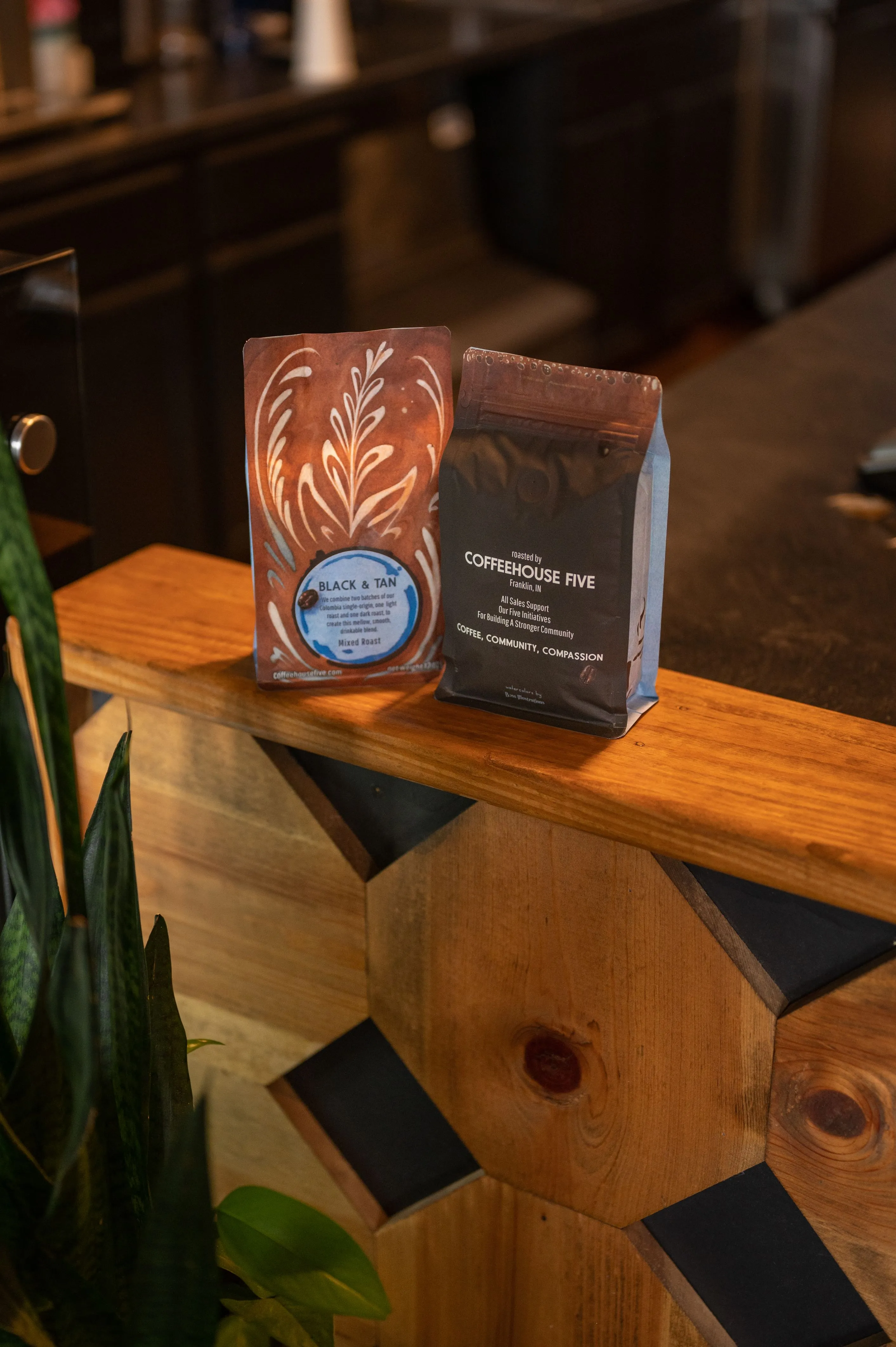 Two bags of artisan coffee on a wooden countertop with a backdrop of a modern cafe interior.