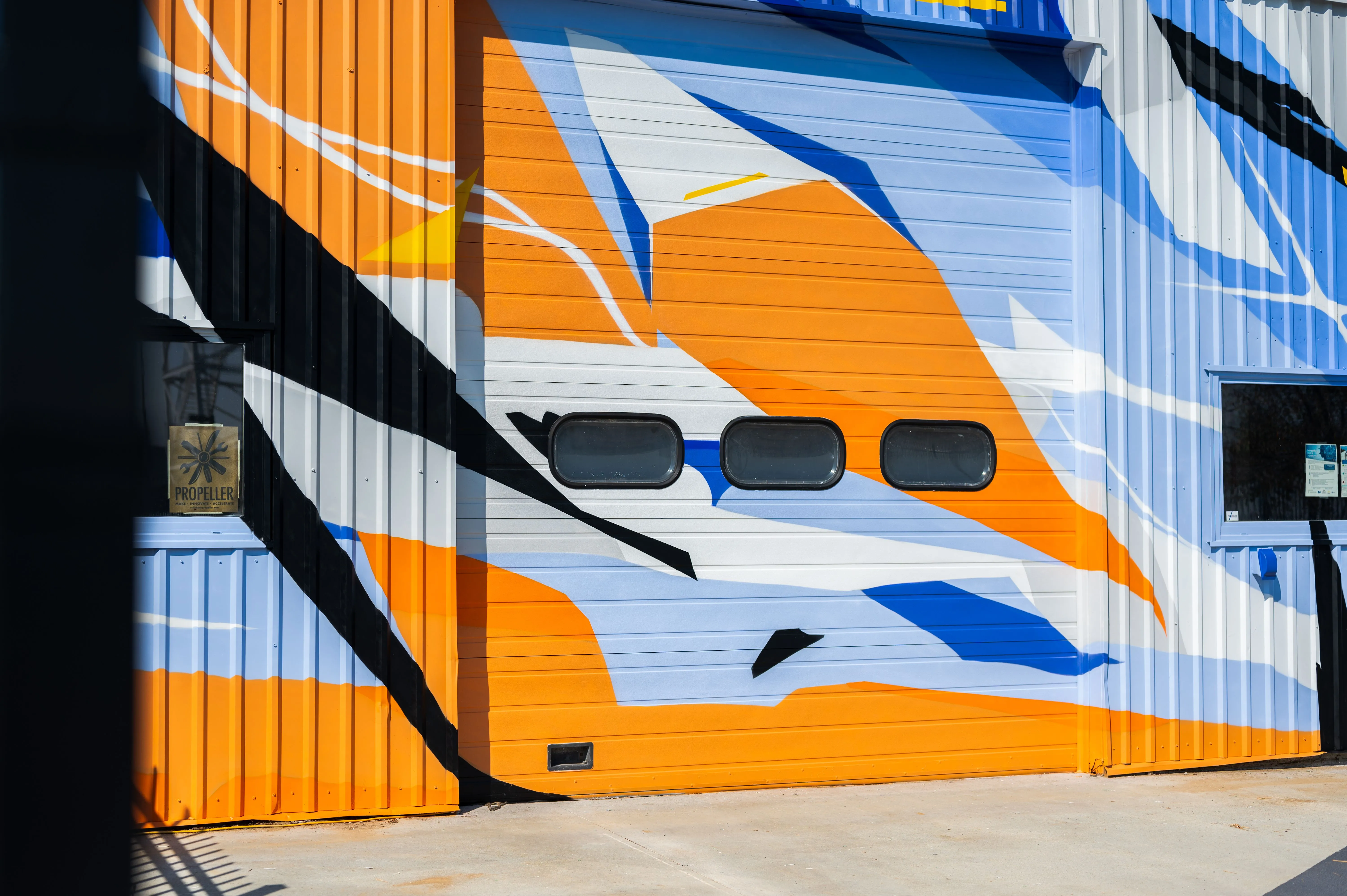 Abstract bird mural on a corrugated metal surface with shadow of stair railings.