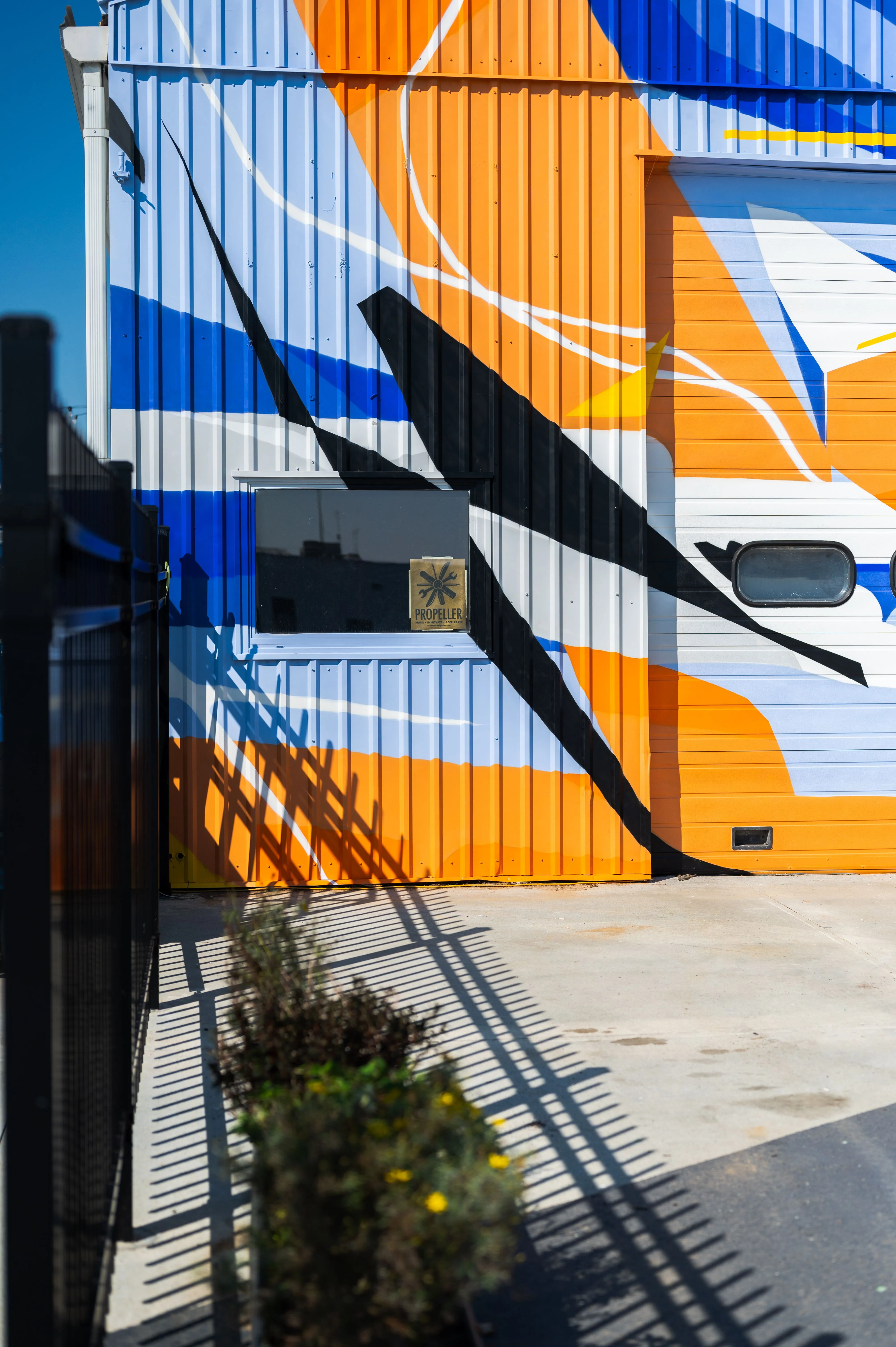 Colorfully painted shipping containers with a staircase shadow cast on the ground and a sign reading "PROPELLER".