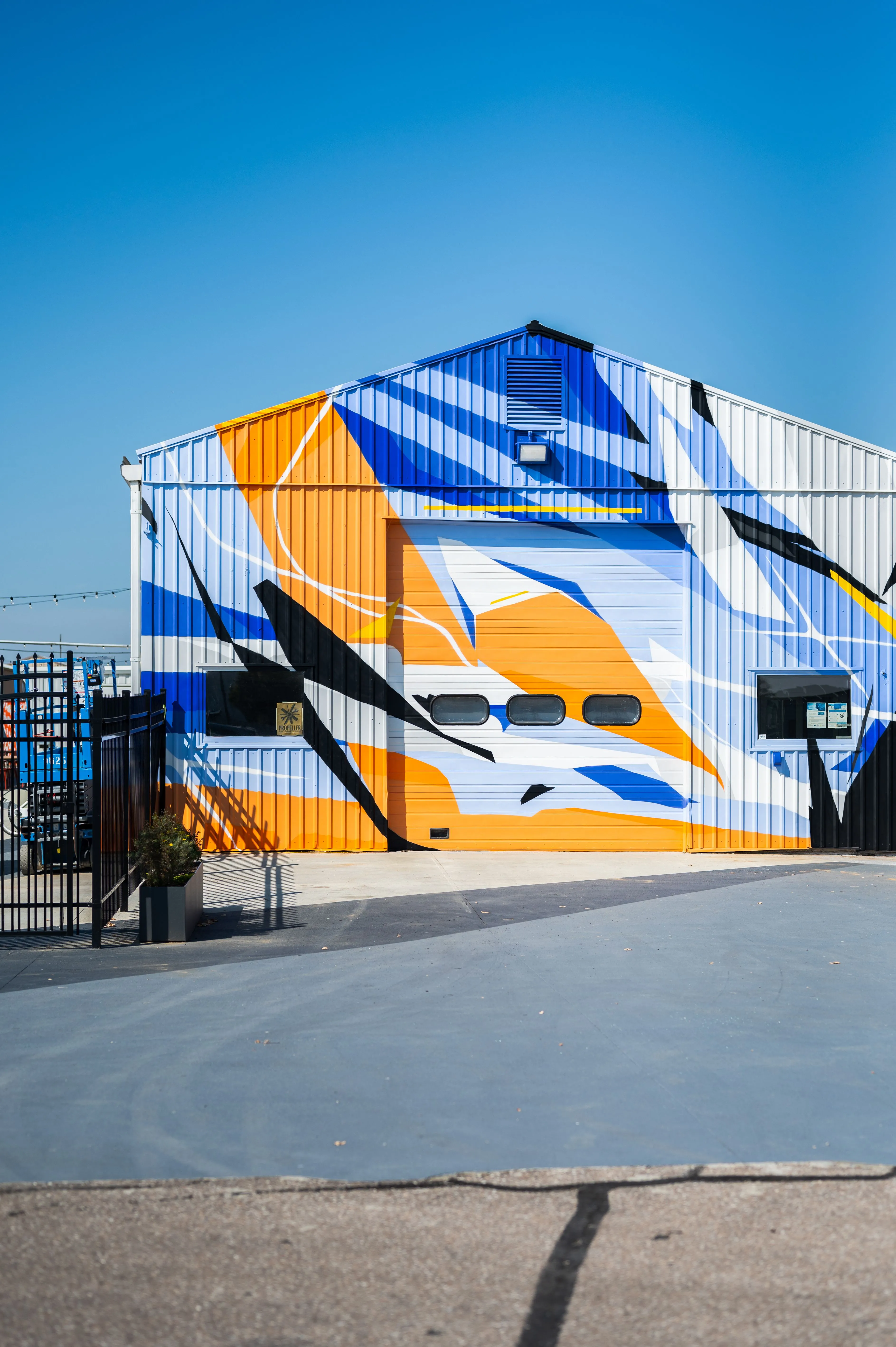 Modern industrial building with a colorful geometric mural on its facade, under a clear blue sky.