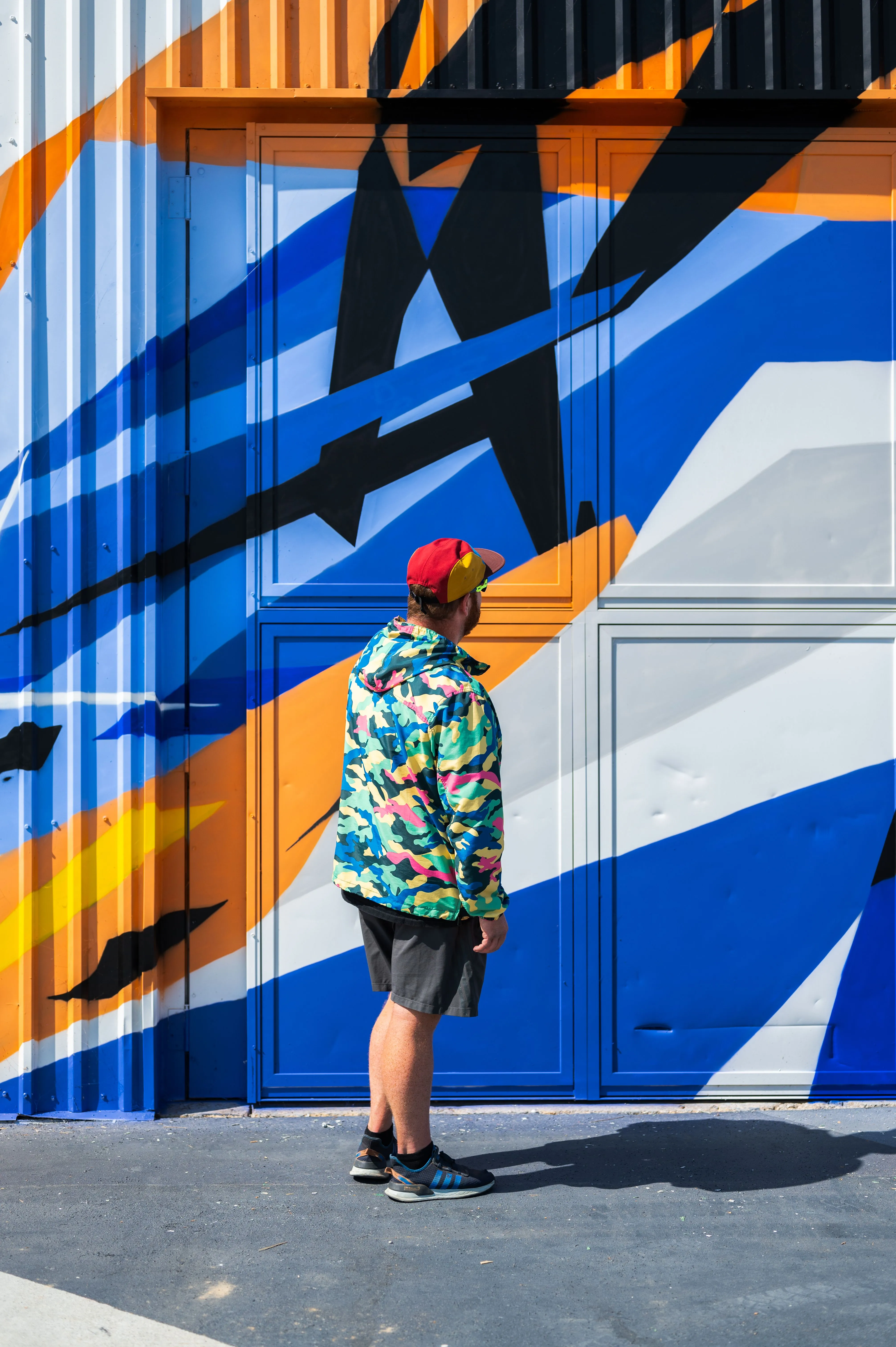 Person standing in front of a colorful geometric mural painted on shipping containers.