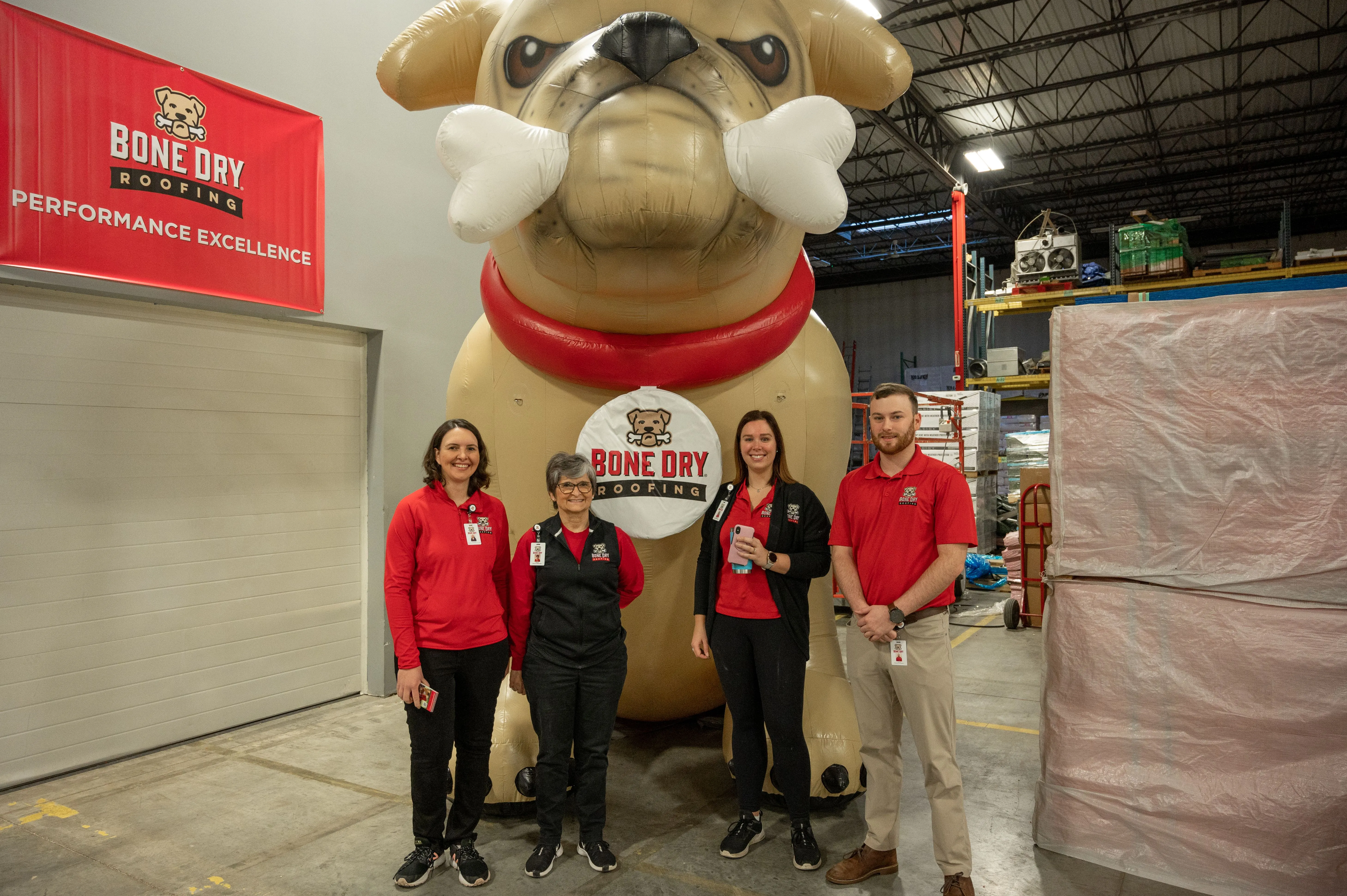 Four people standing in front of a giant inflatable bulldog mascot inside a warehouse.