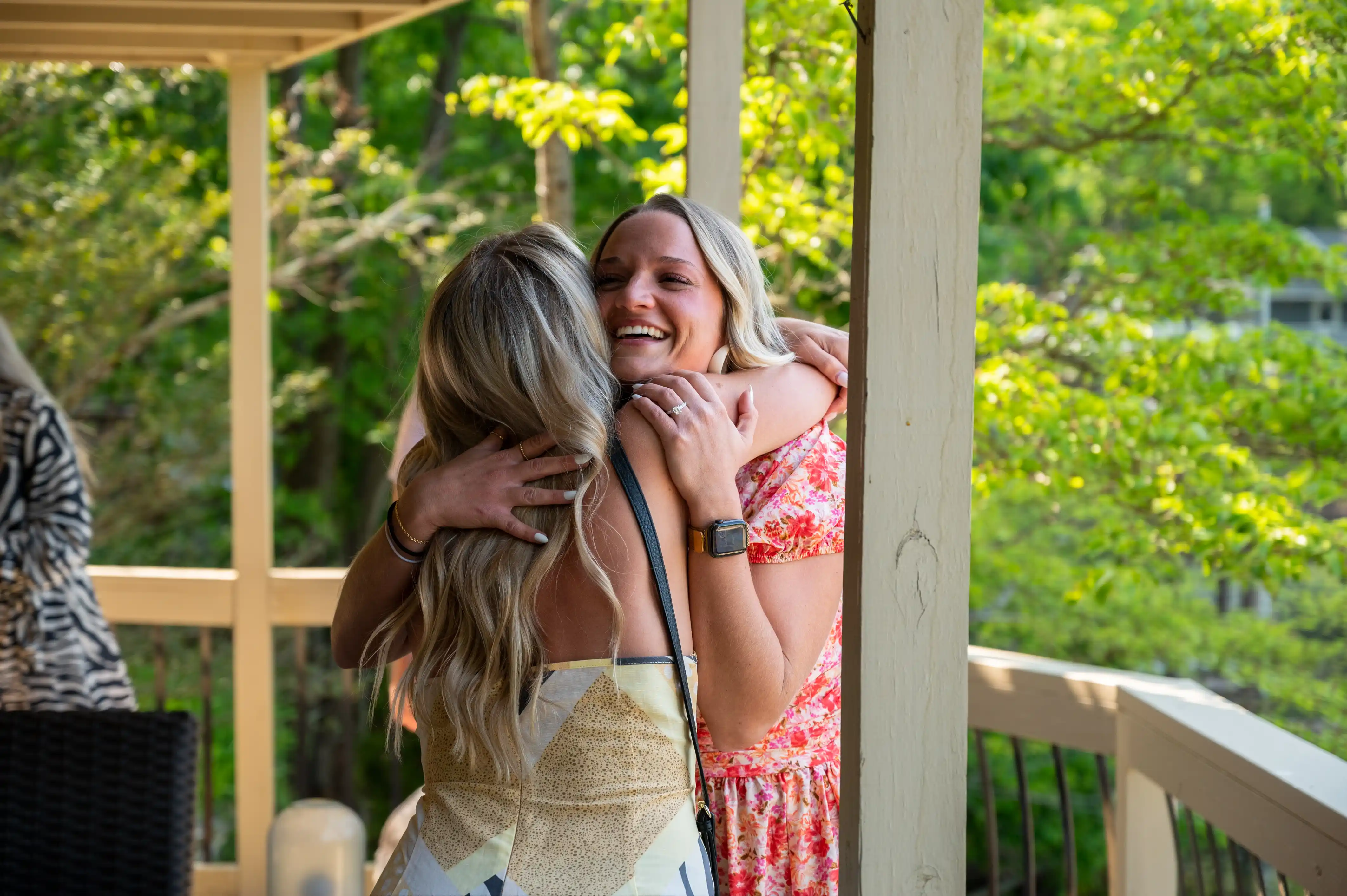 Two women embracing in a happy hug on a porch with trees in the background.