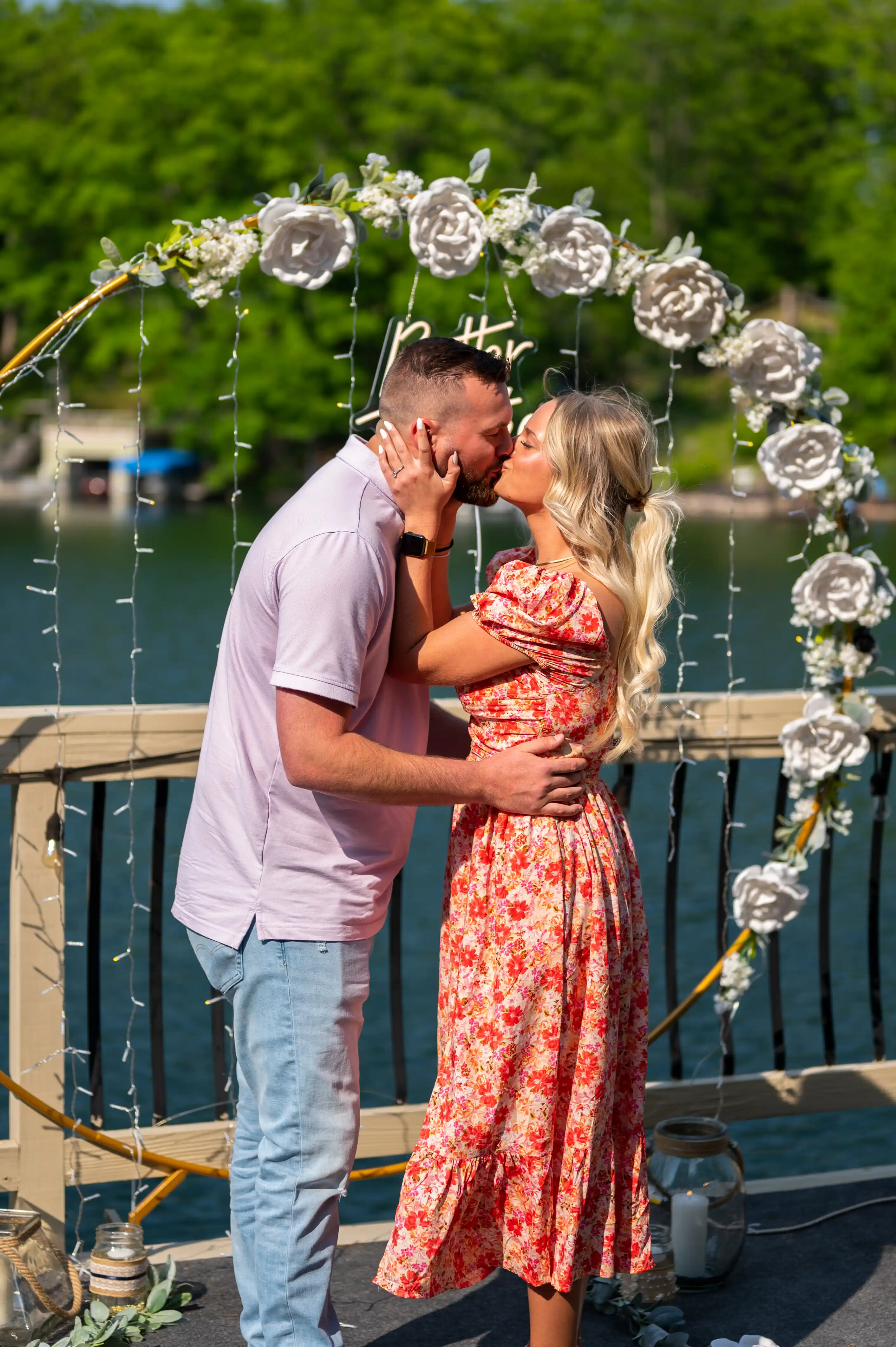 Couple kissing under a floral arch on a sunny day.