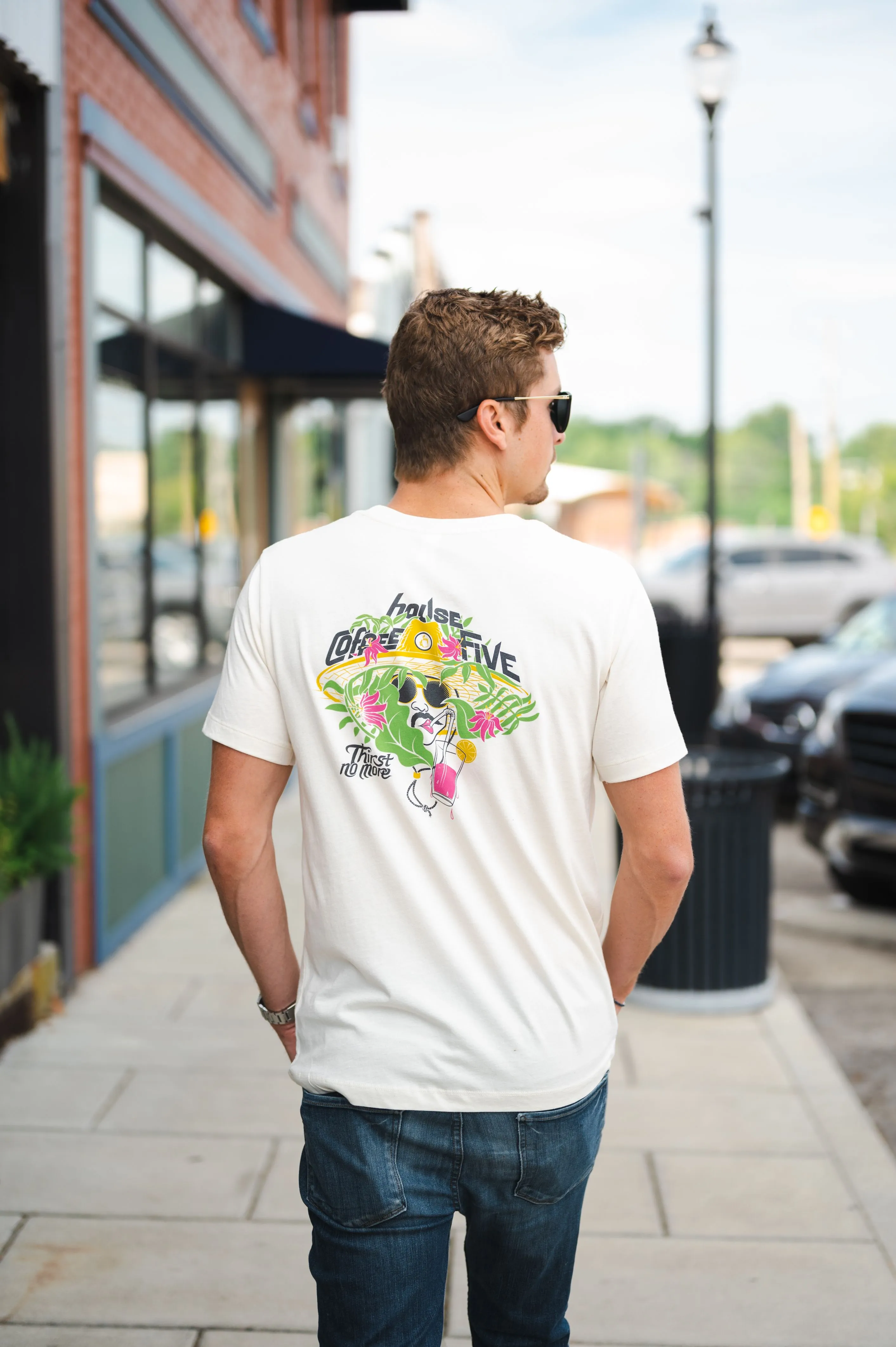 Man wearing white t-shirt with colorful back print and sunglasses walking on a city sidewalk.