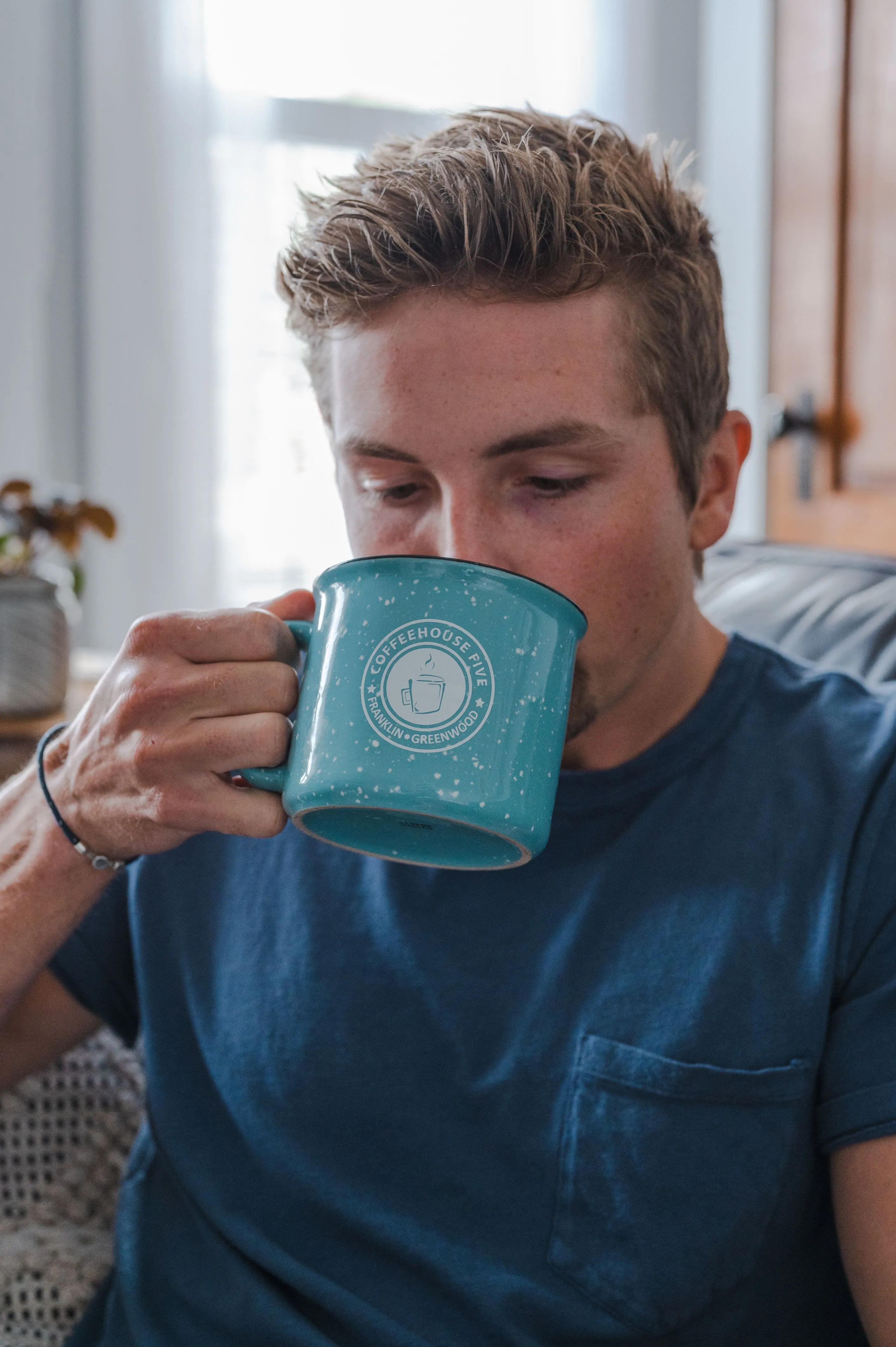 Young man drinking from a turquoise coffee mug indoors.