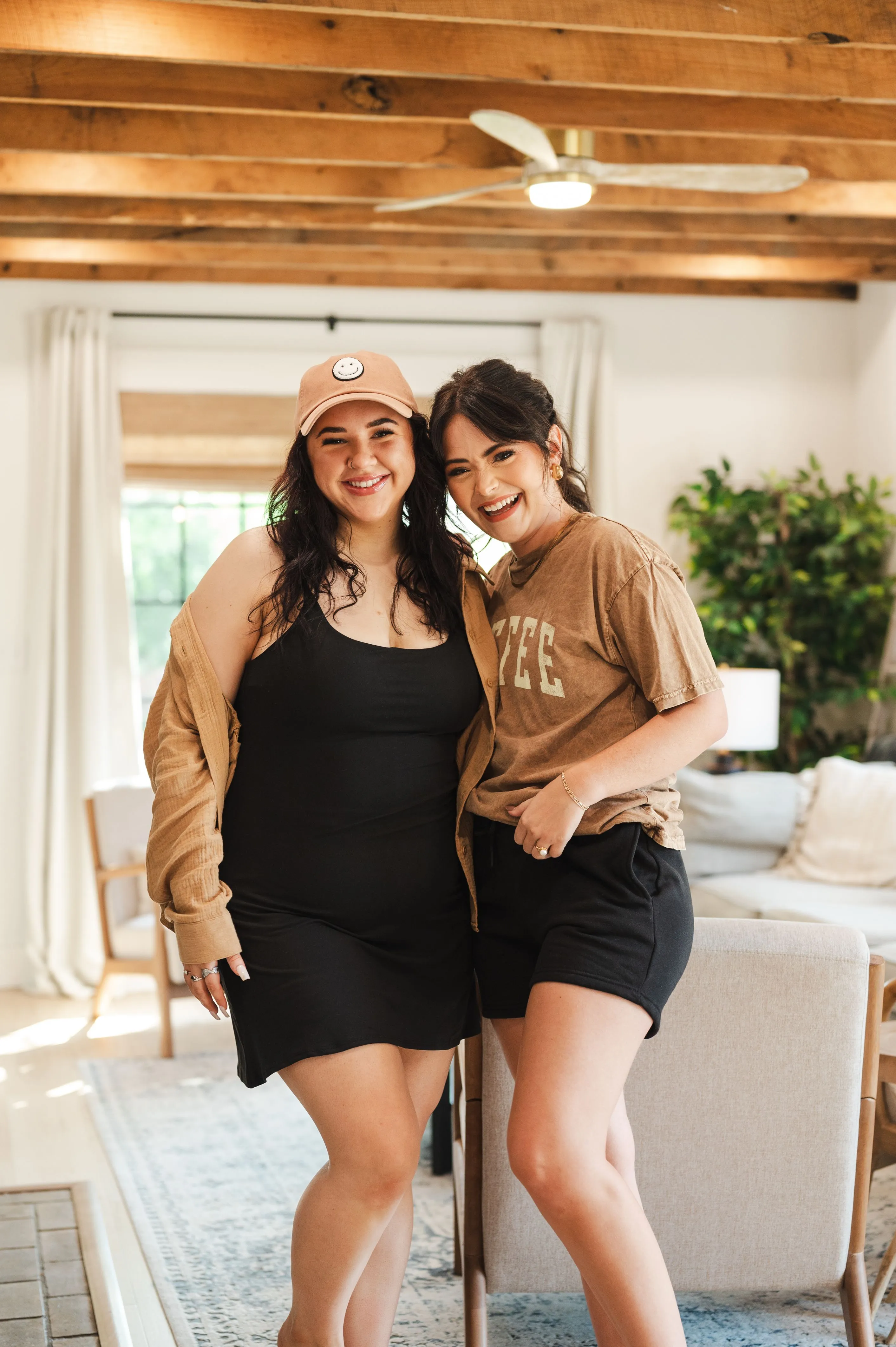 Two smiling women standing together with arms around each other in a cozy living room setting.