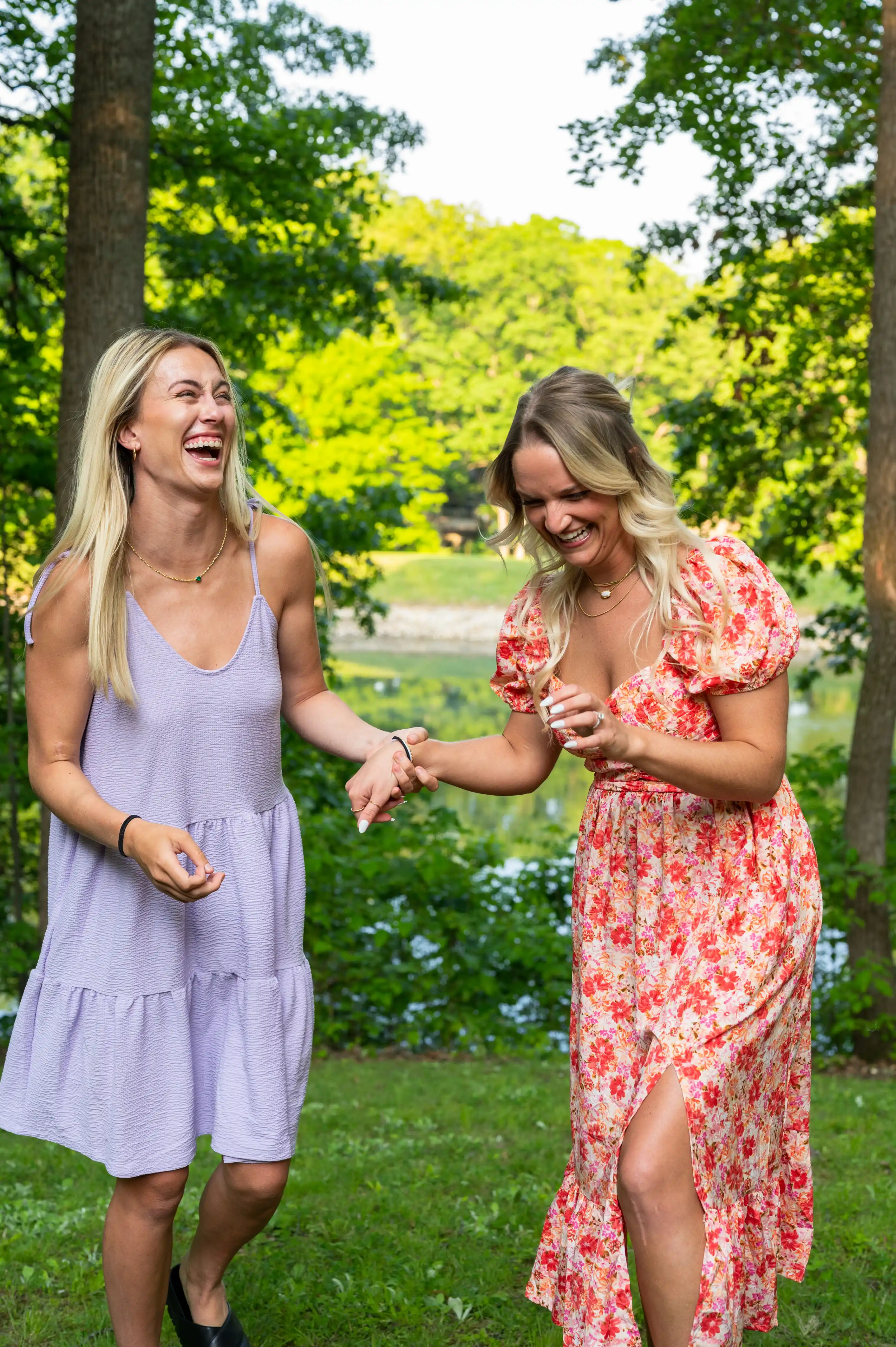 Two women laughing and walking in a park with trees in the background.