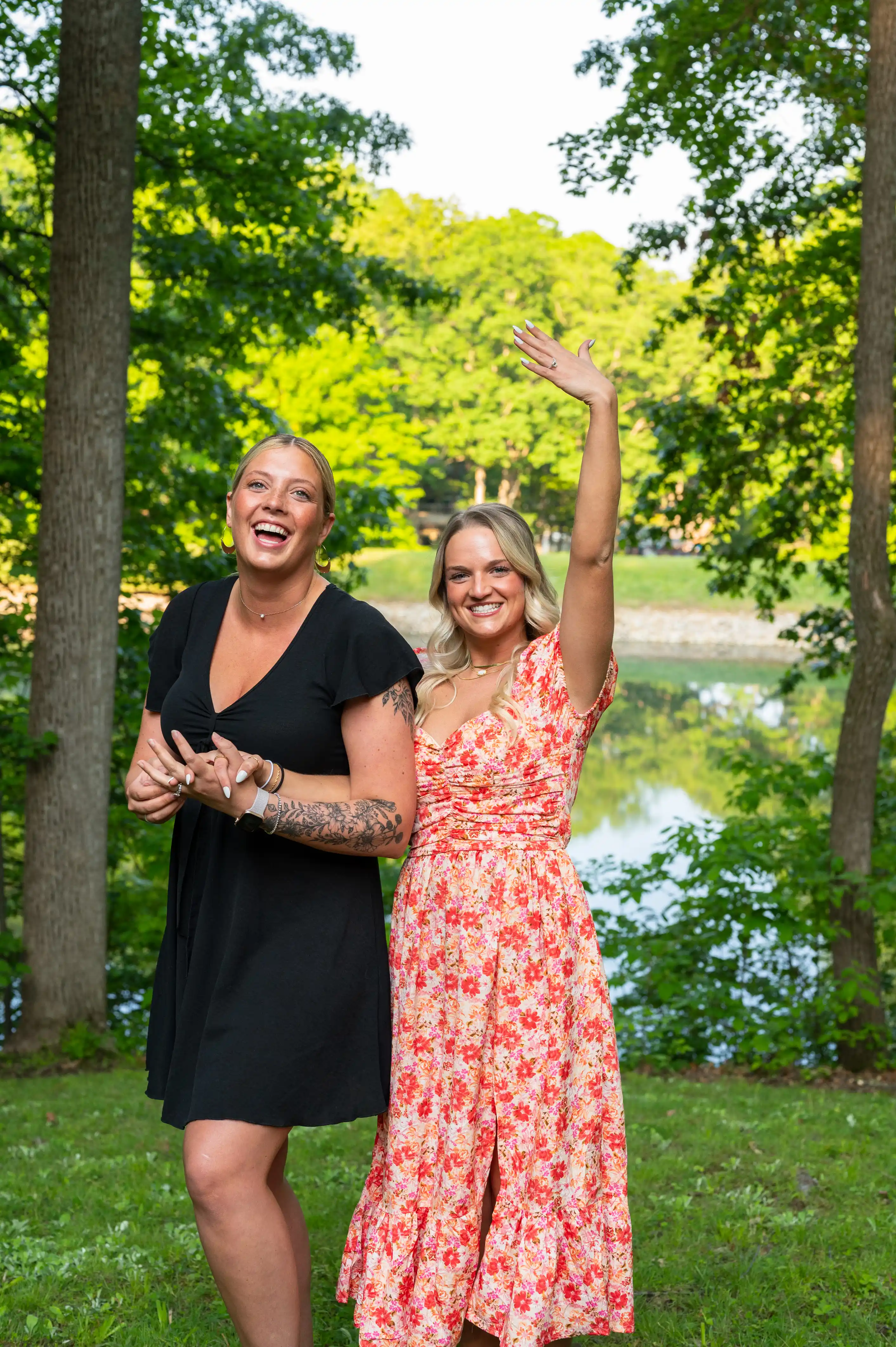 Two women smiling and celebrating in a park with one woman raising her arm in the air.