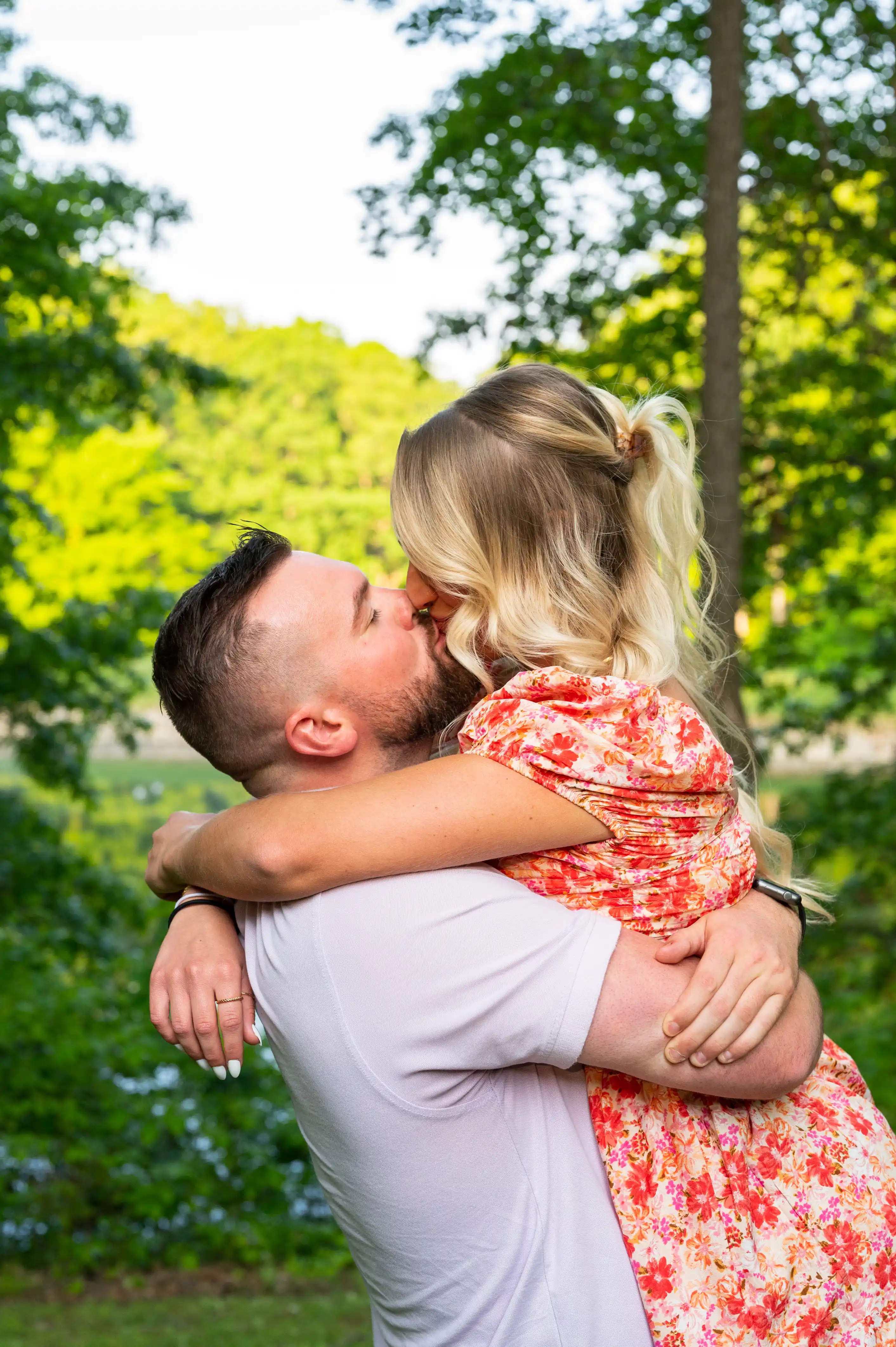 Father embracing young daughter with affection outdoors with greenery in the background.