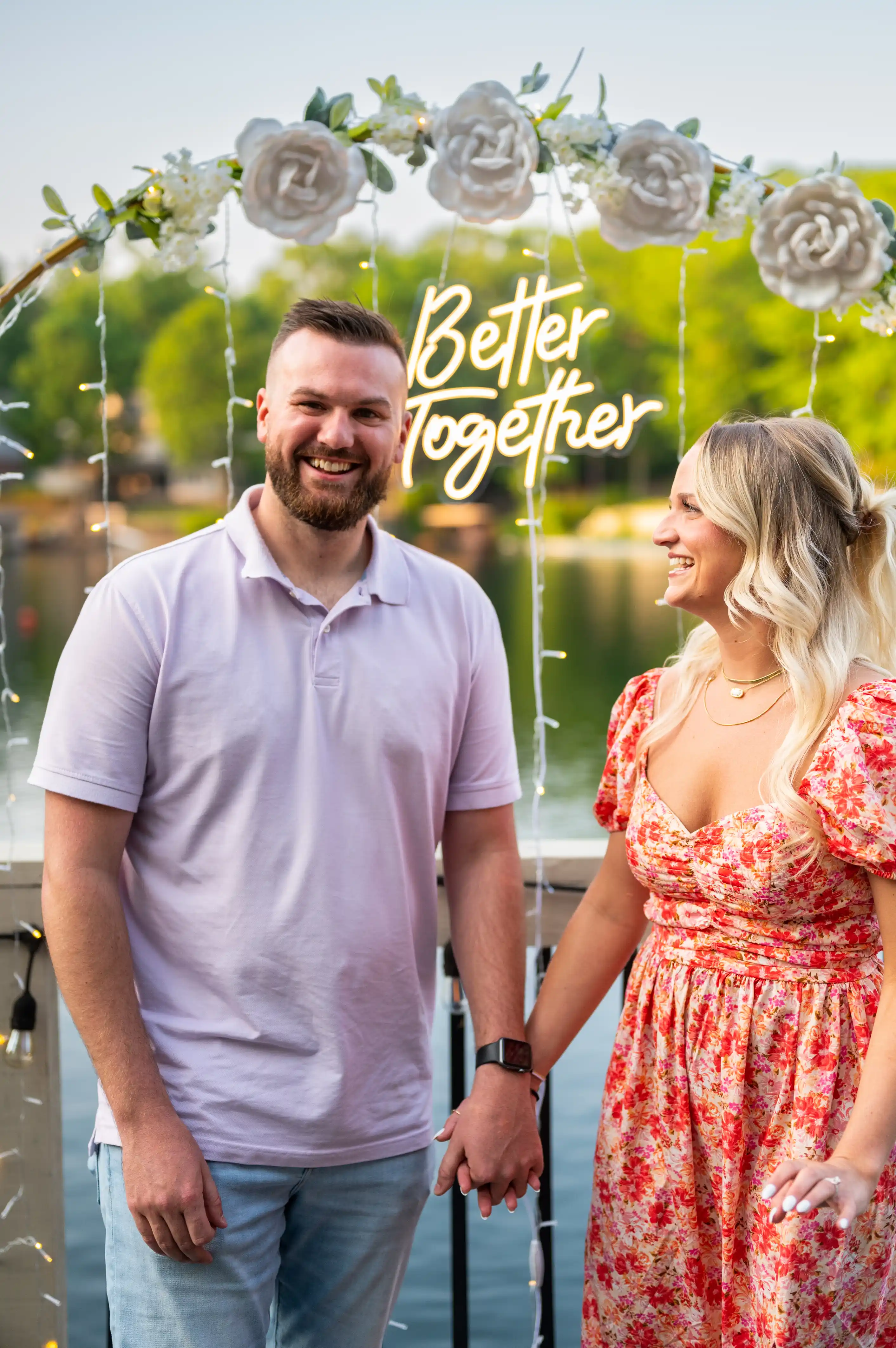 A smiling couple standing by a lake with a "Better Together" sign floating above their heads.