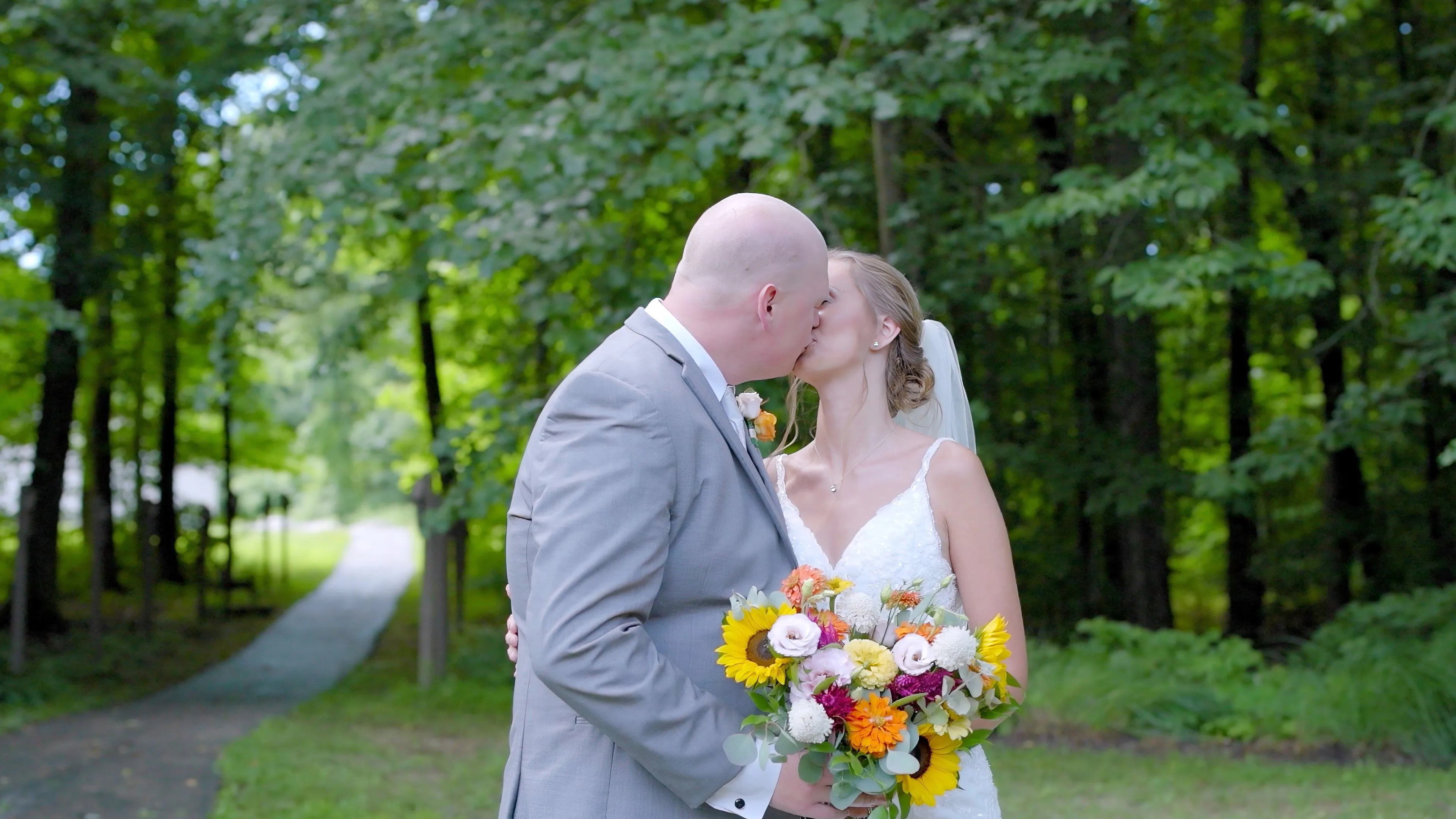 A bride and groom sharing a kiss outdoors, surrounded by greenery, with the bride holding a bouquet of flowers.