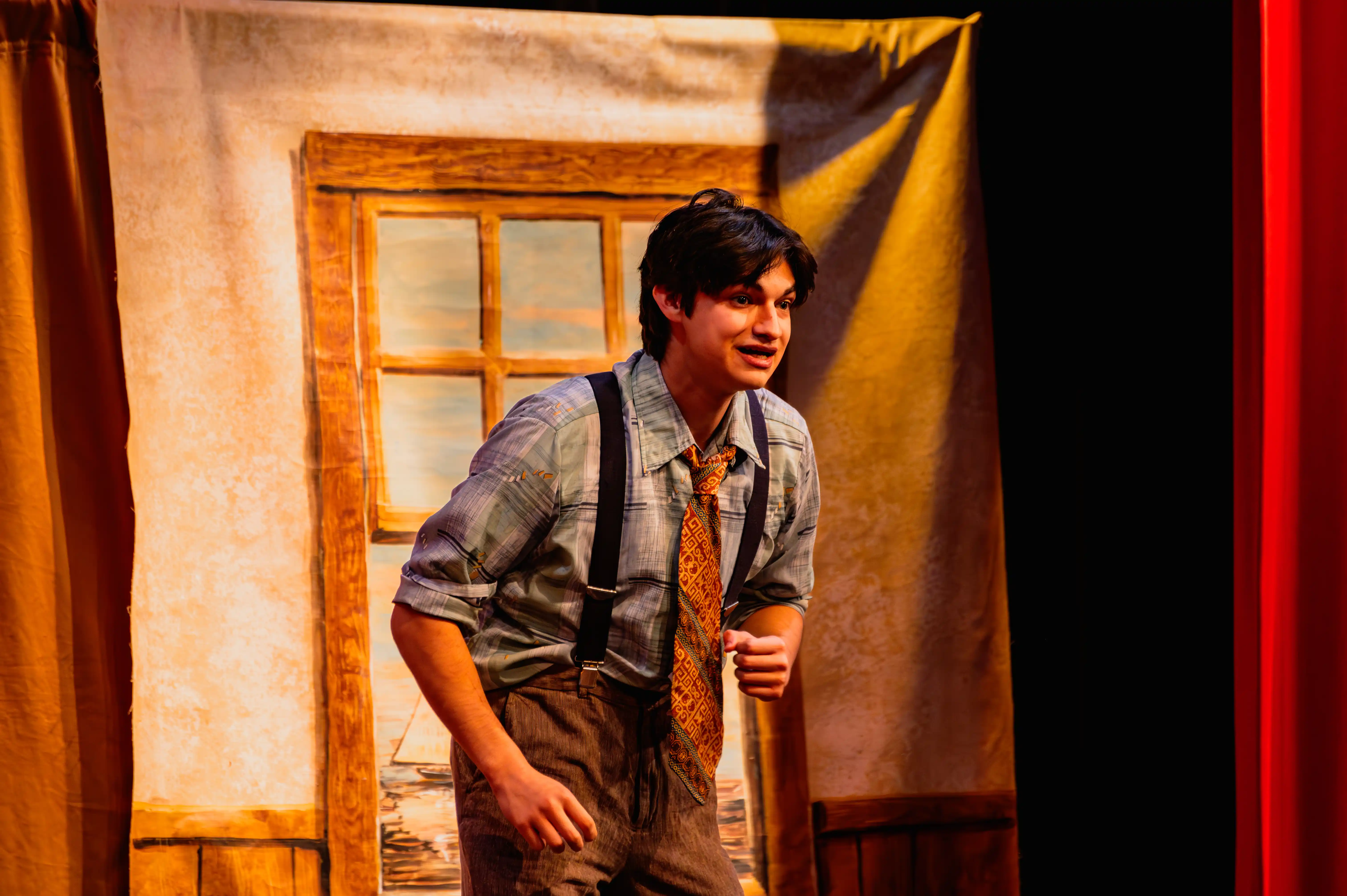 Actor on stage performing in a play with a painted backdrop of a window.