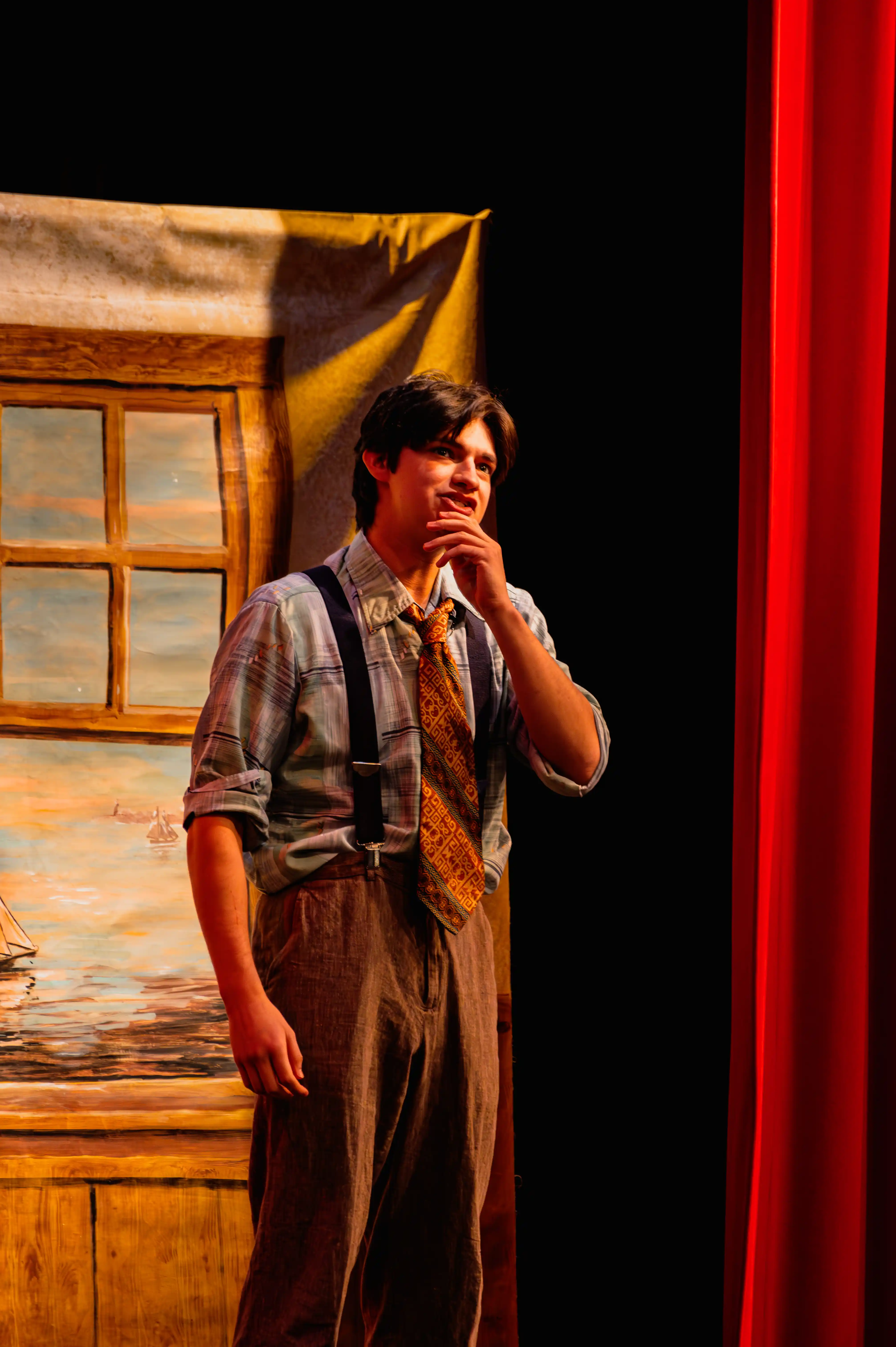 Actor in period costume performing on stage with thoughtful expression, standing beside a painted door backdrop.